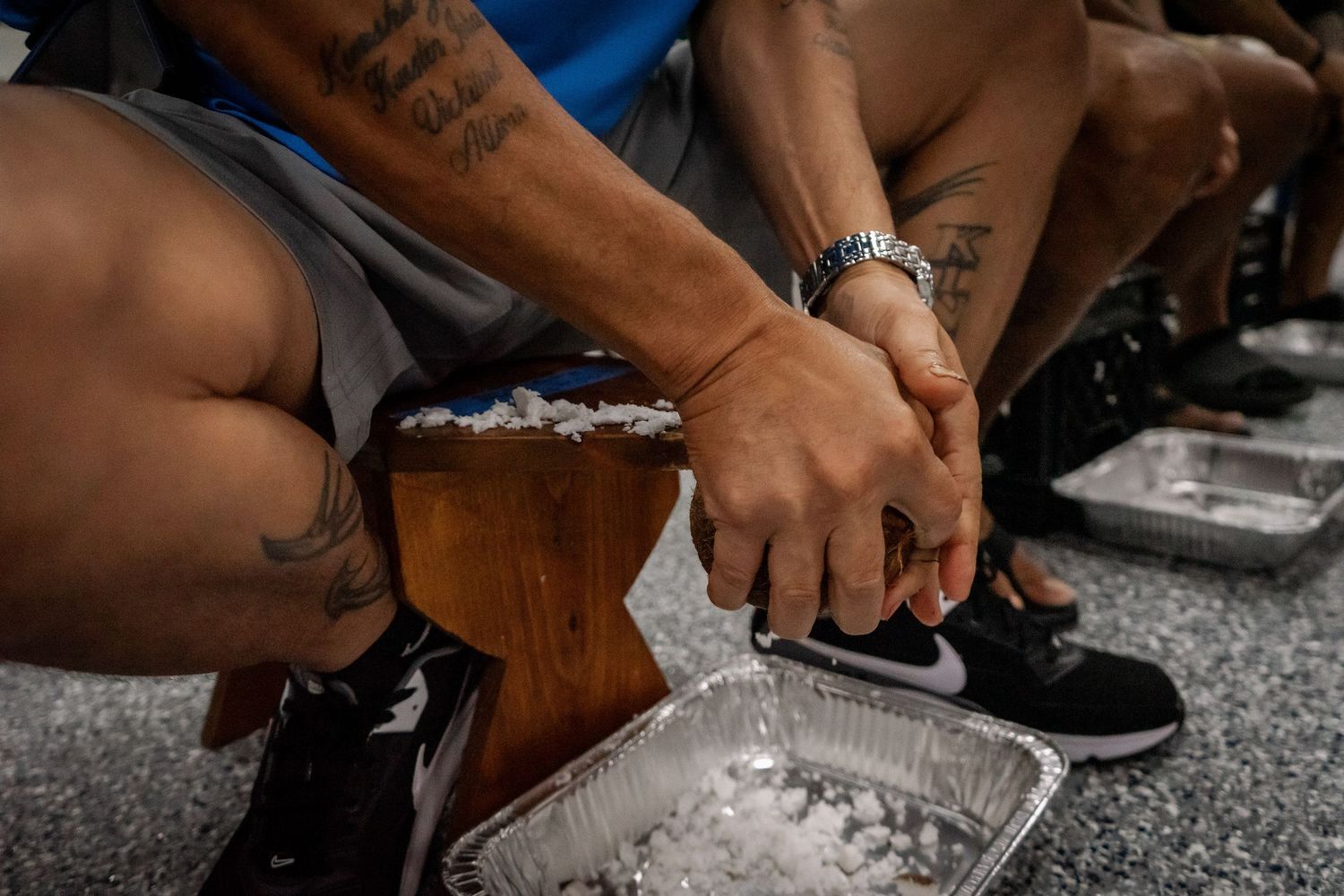People with tattoos sit together holding hands over aluminum trays of rice.
