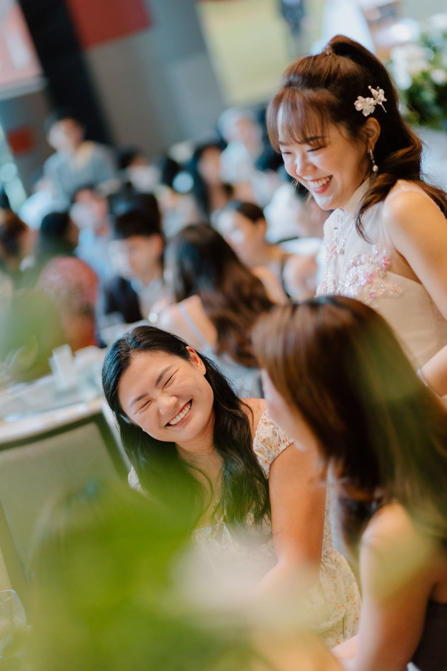 Joyful Asian women laughing together at a wedding reception banquet.