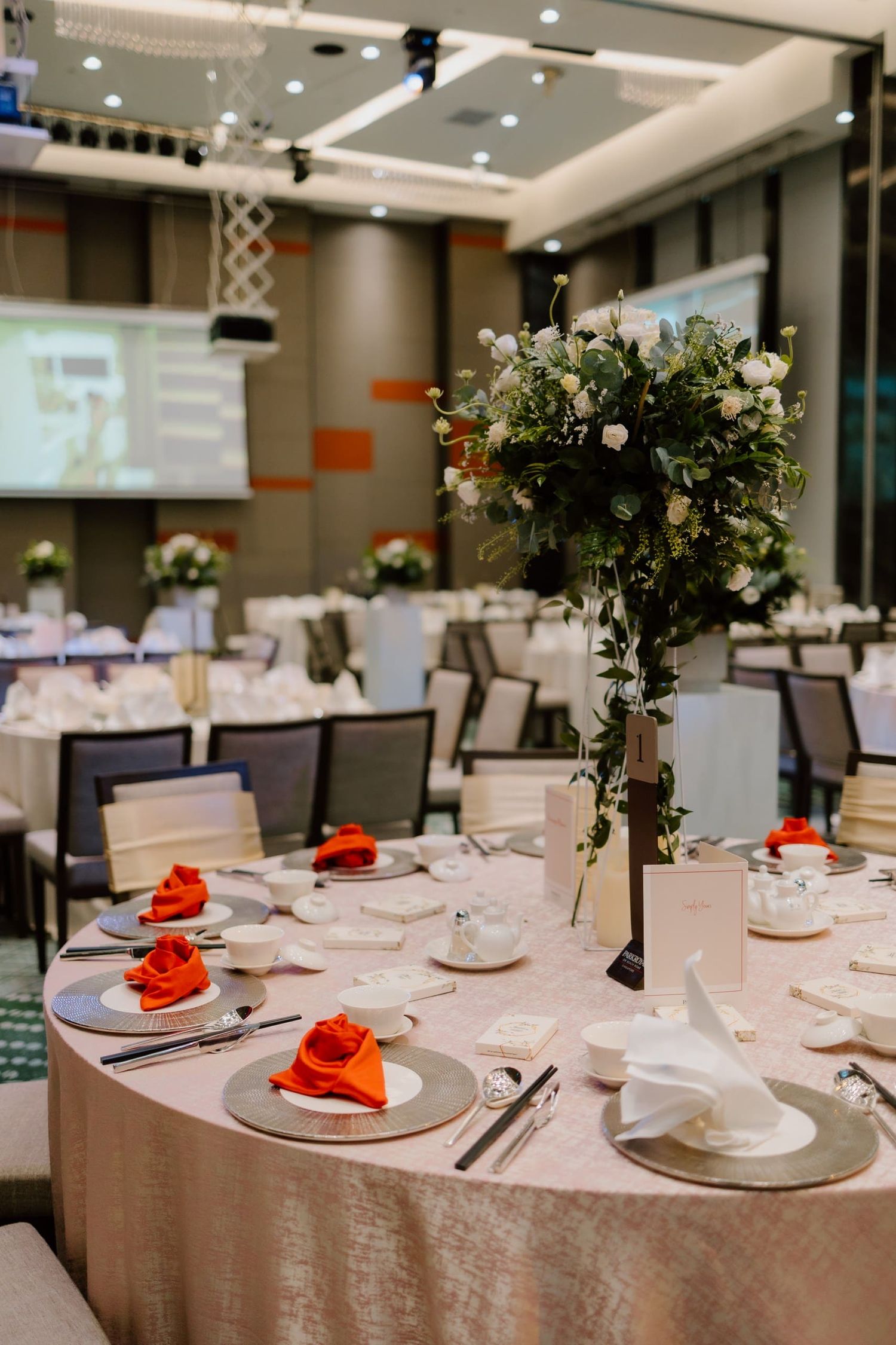 Elegant banquet hall with round tables set with red napkins and tall floral centerpieces for a formal event.