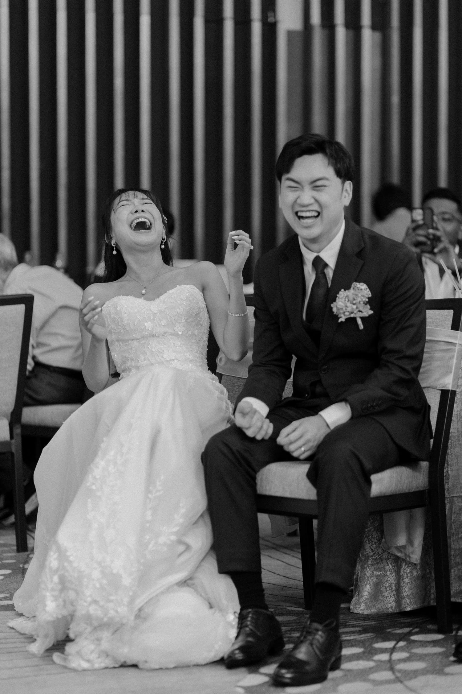Black and white photo of a bride and groom laughing joyfully together at their wedding reception.