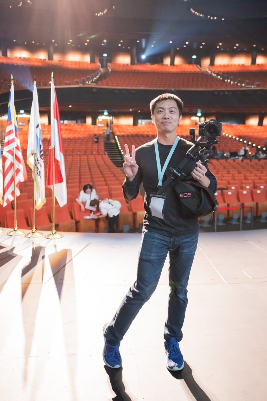 Videographer posing with Canon camera in large auditorium venue.