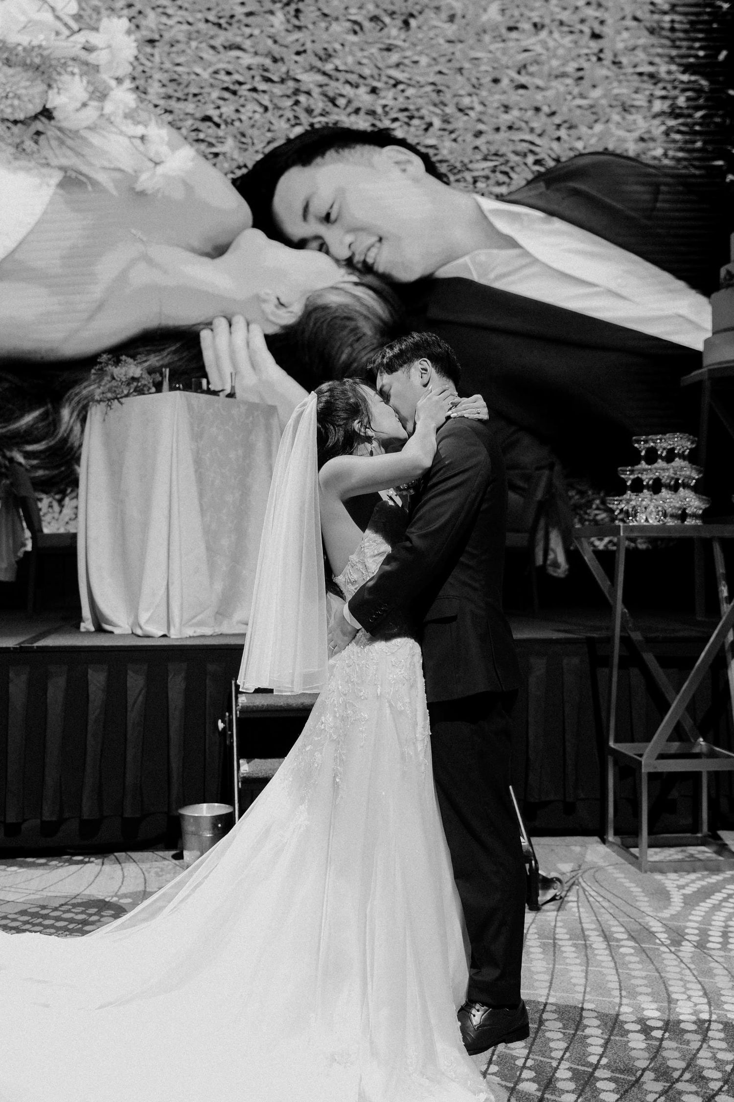 Black and white wedding photo of bride and groom sharing first kiss, with romantic double exposure effect.
