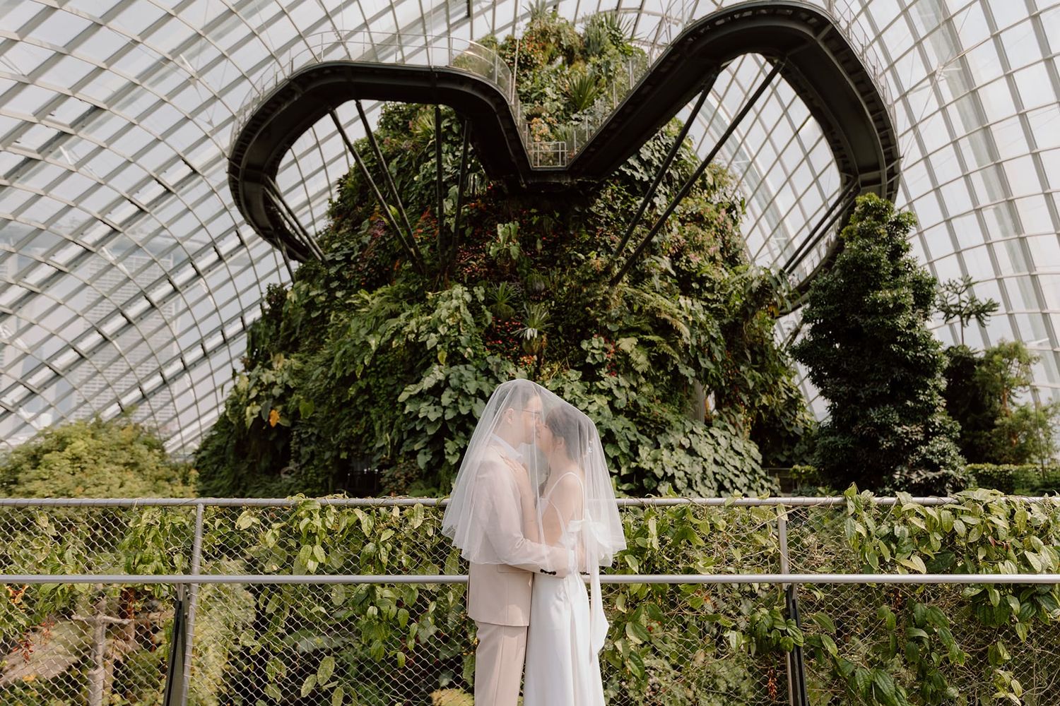 A tender moment captured under a glass dome conservatory with arching architectural details.