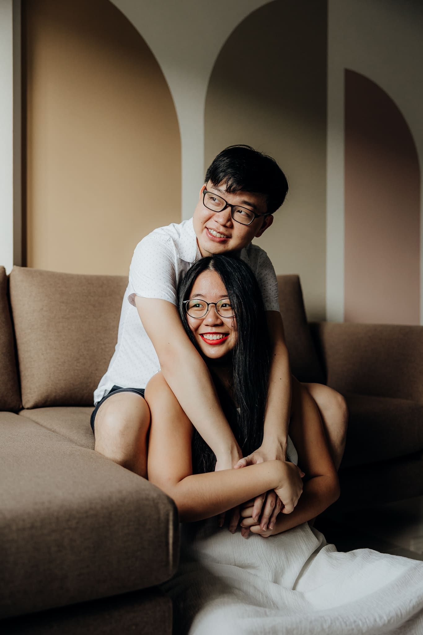 Intimate couple shares tender moments on a brown couch in natural lighting.