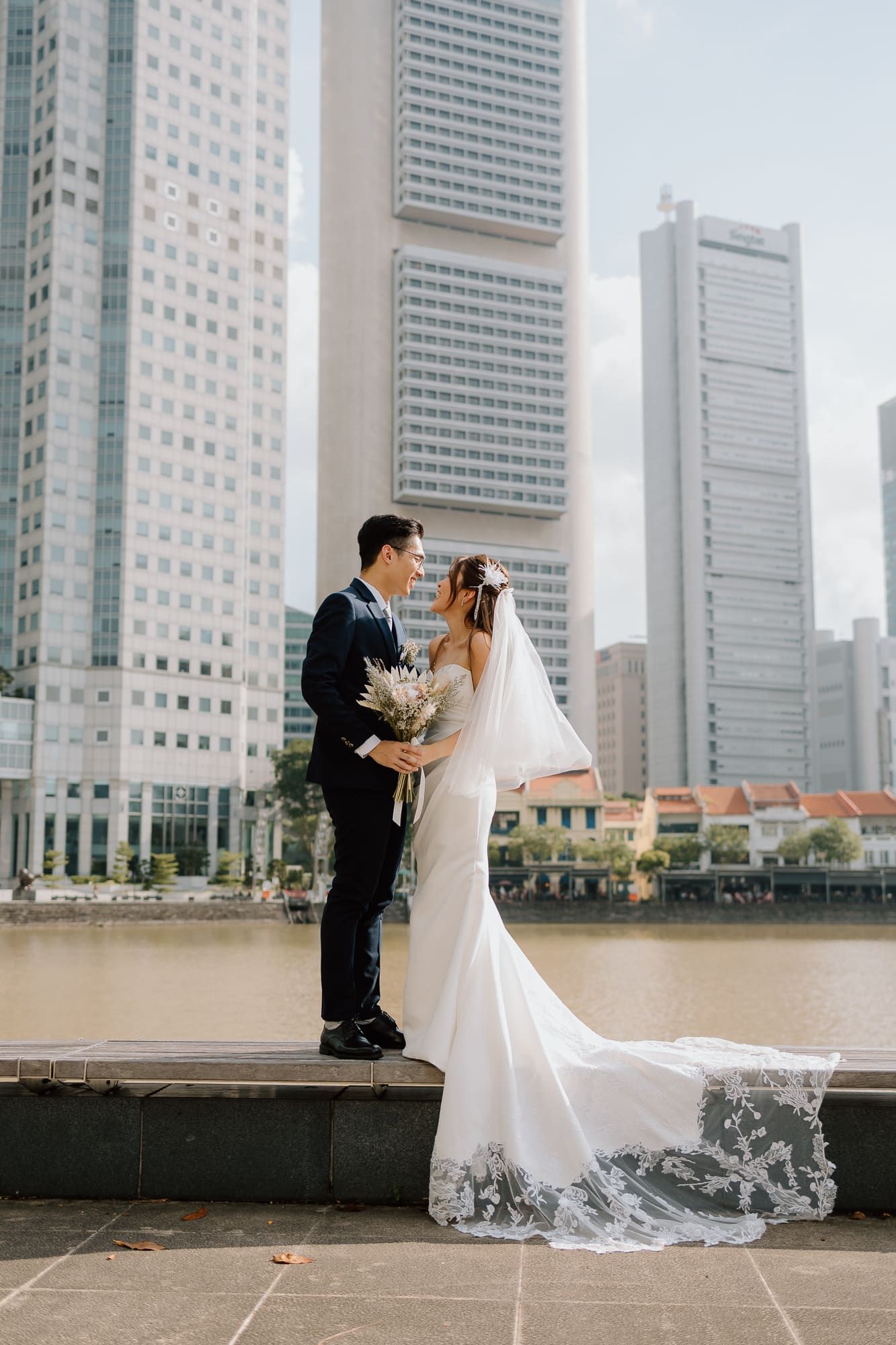 Couple in wedding attire embraces against a backdrop of modern skyscrapers in Singapore's city center.