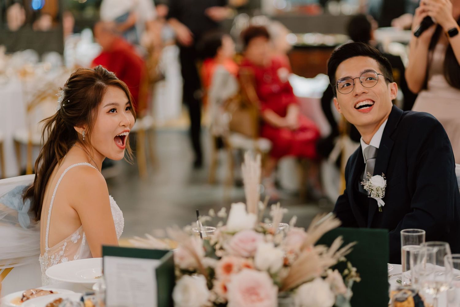 Wedding reception scene showing two enthusiastic guests sharing a joyful candid moment at a decorated dining table.