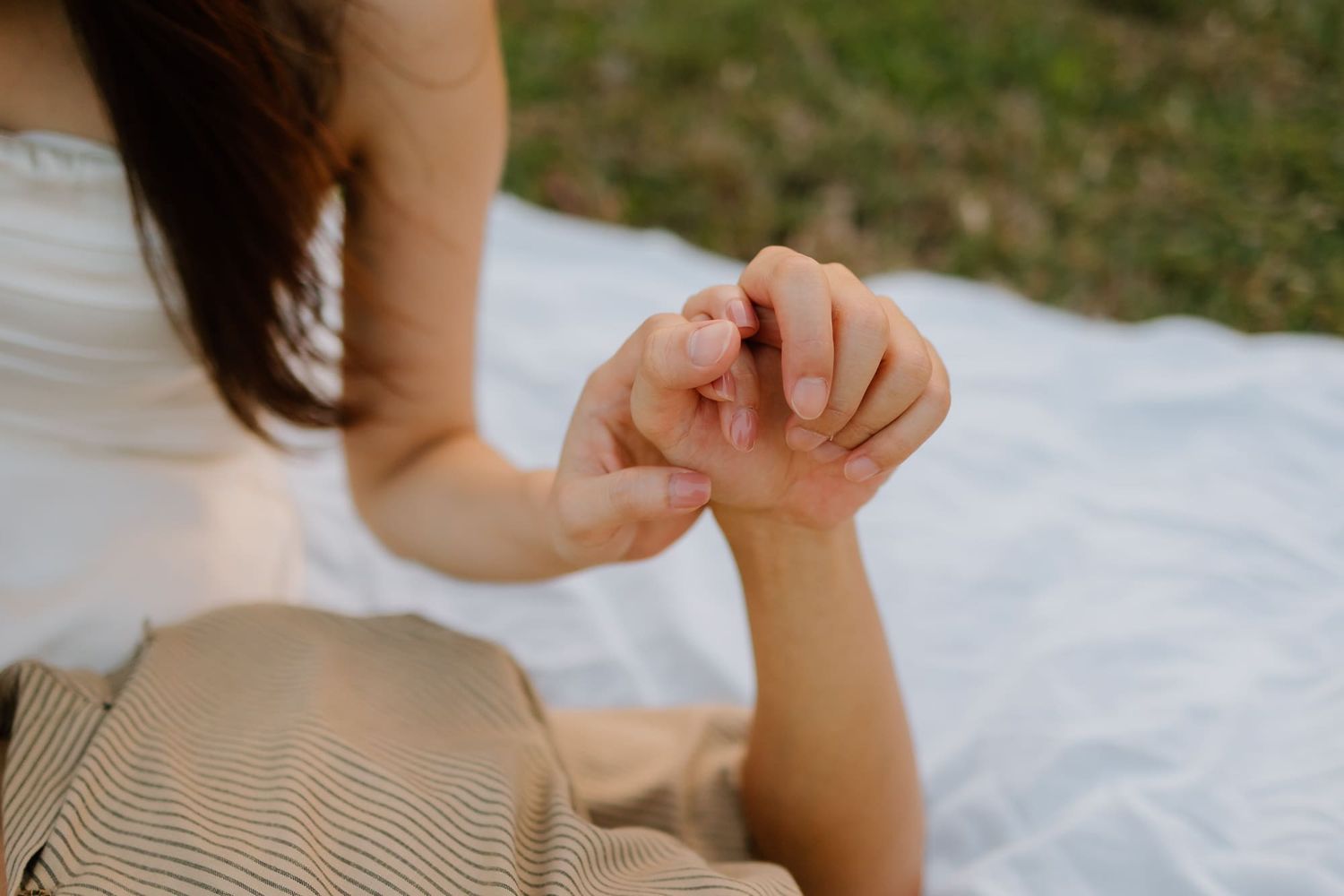 Couple holding hands gently on a white blanket outdoors, romantic connection and togetherness.
