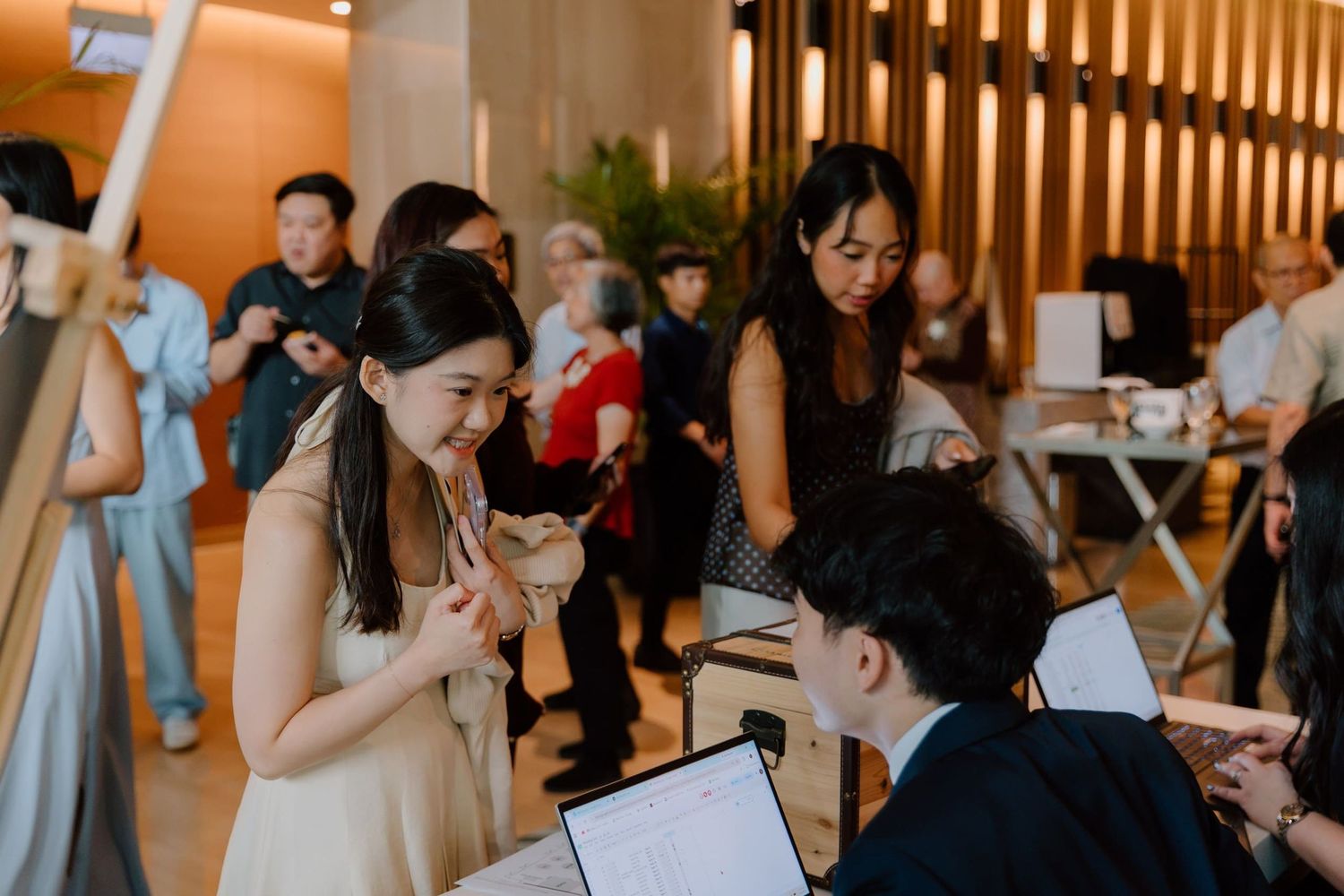 A smiling woman in a white dress chats with a seated guest at an elegant indoor social gathering event.