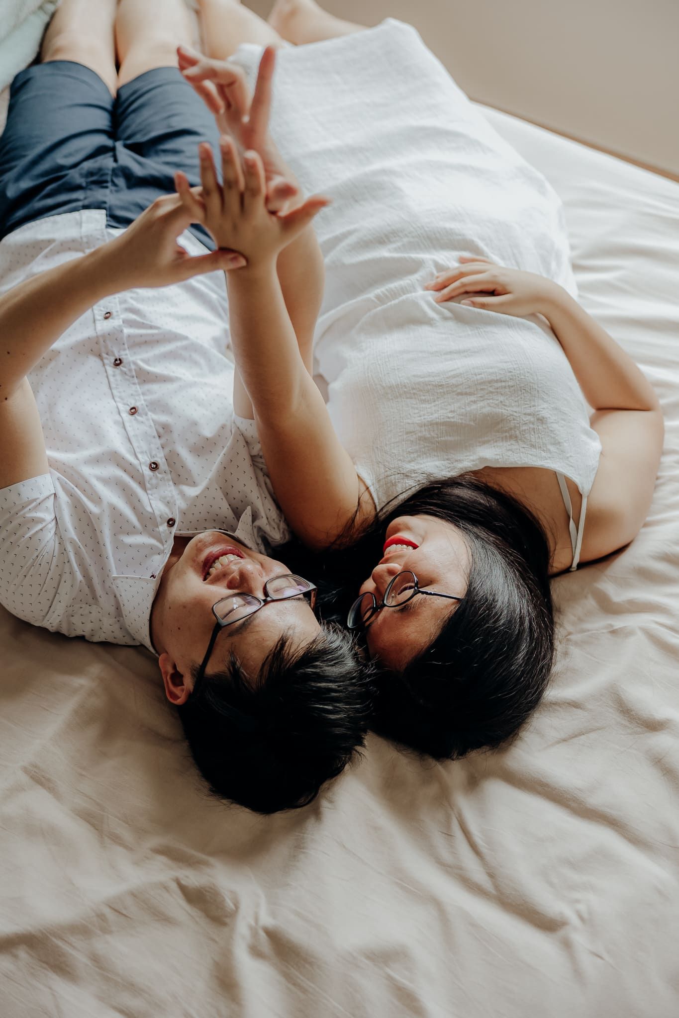 Two people share playful moments while relaxing on clean white bedding.