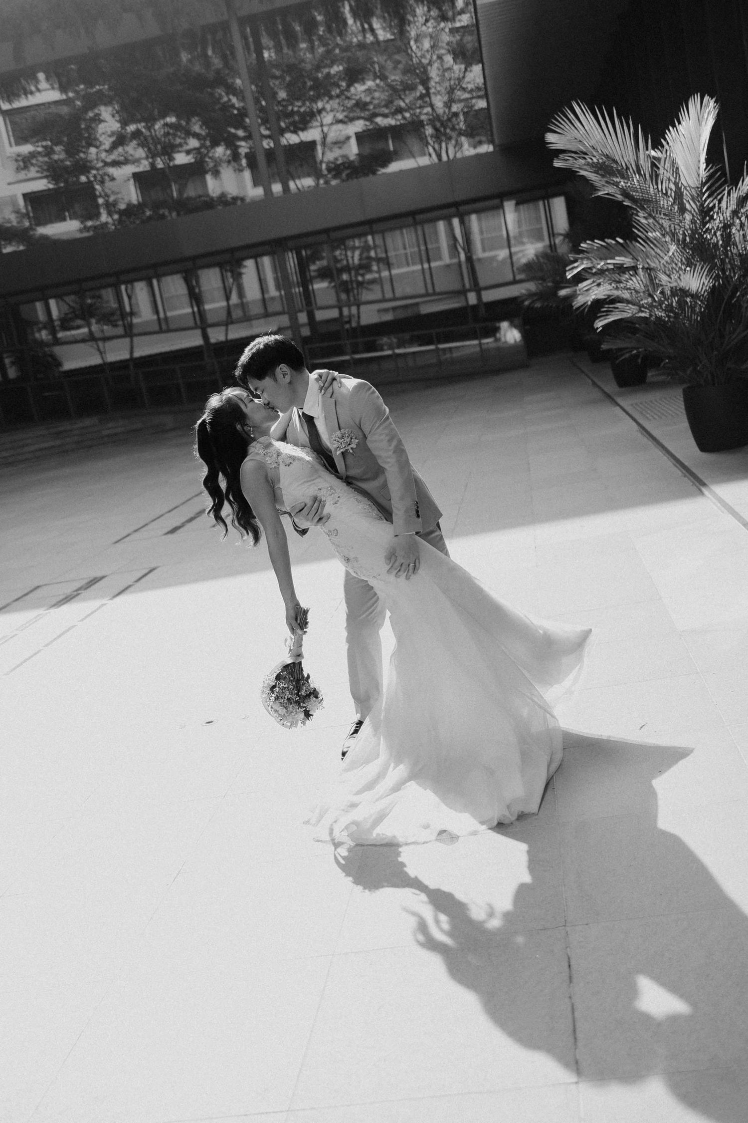 Black and white photo of bride and groom sharing a romantic dip kiss outdoors on wedding day.