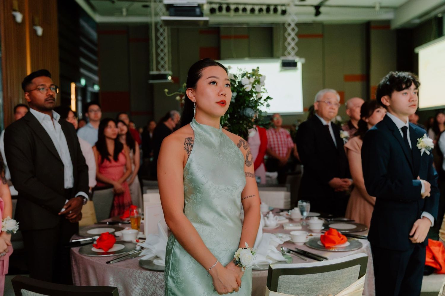 Guests in formal attire stand attentively at an elegant banquet hall during a wedding reception ceremony.