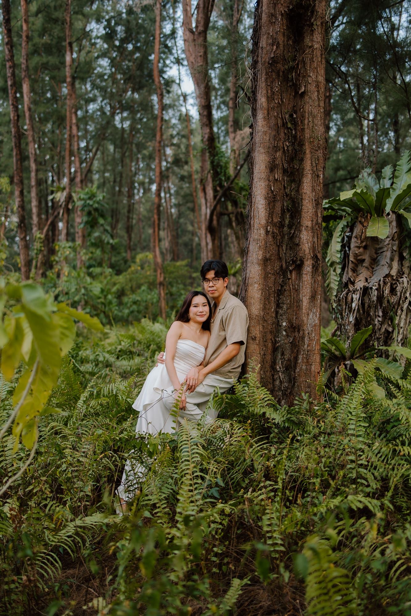 Couple posing romantically in a lush forest surrounded by ferns and tall trees in a nature photoshoot.