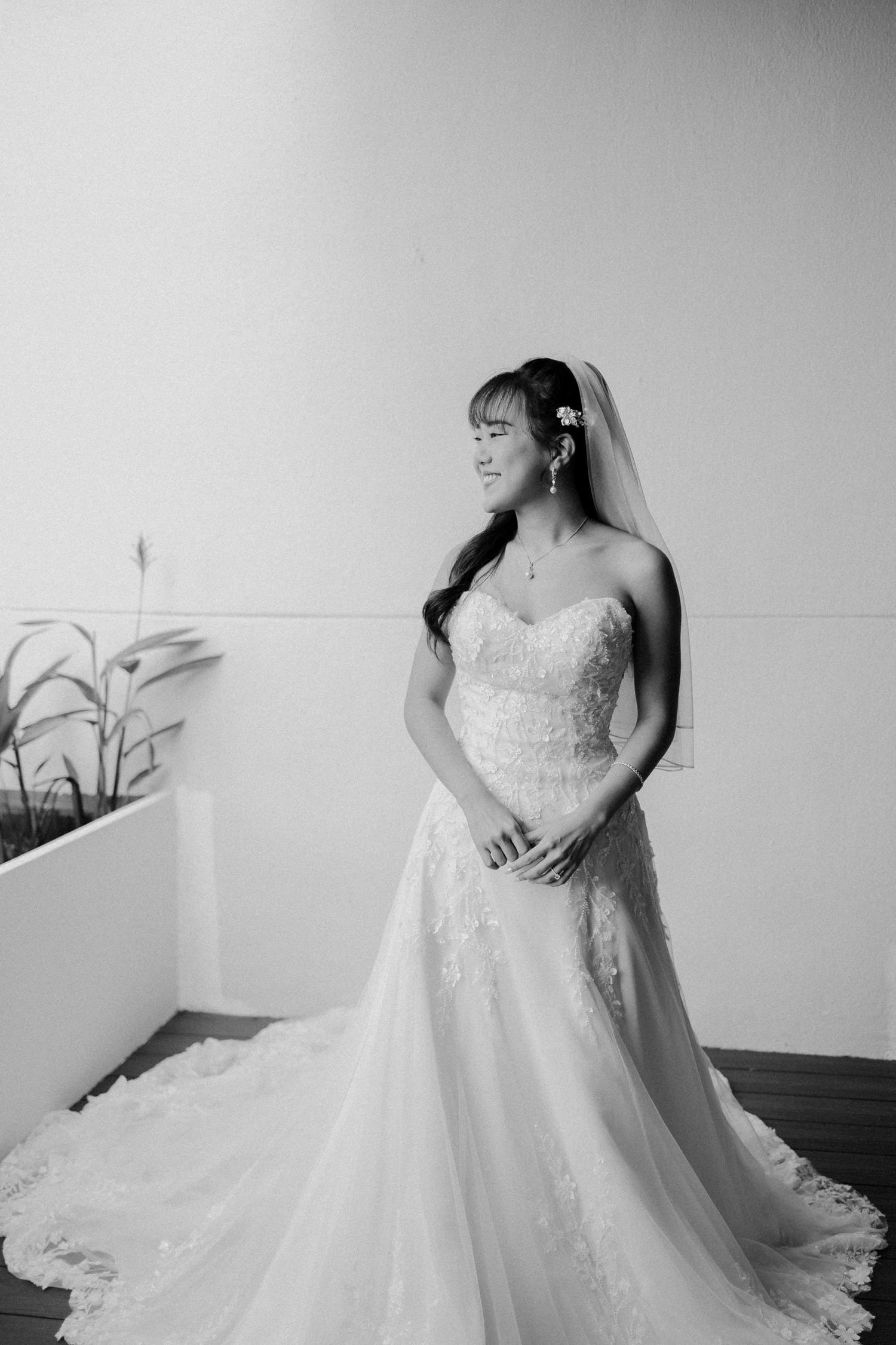 Black and white photo of a bride in a strapless lace A-line wedding gown with veil, smiling softly indoors.
