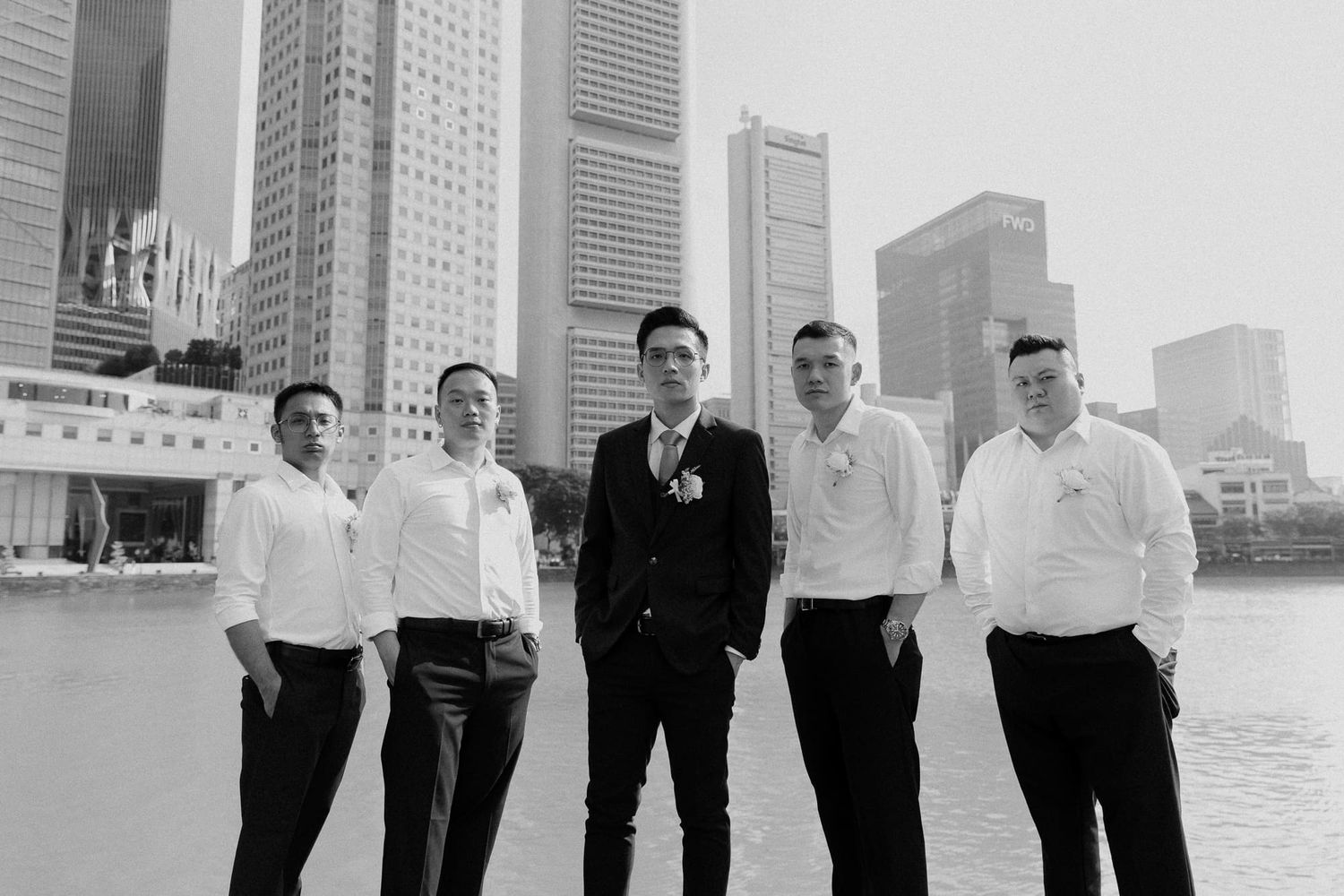 A group of five people in formal attire stand together against a cityscape backdrop with tall buildings in Singapore.