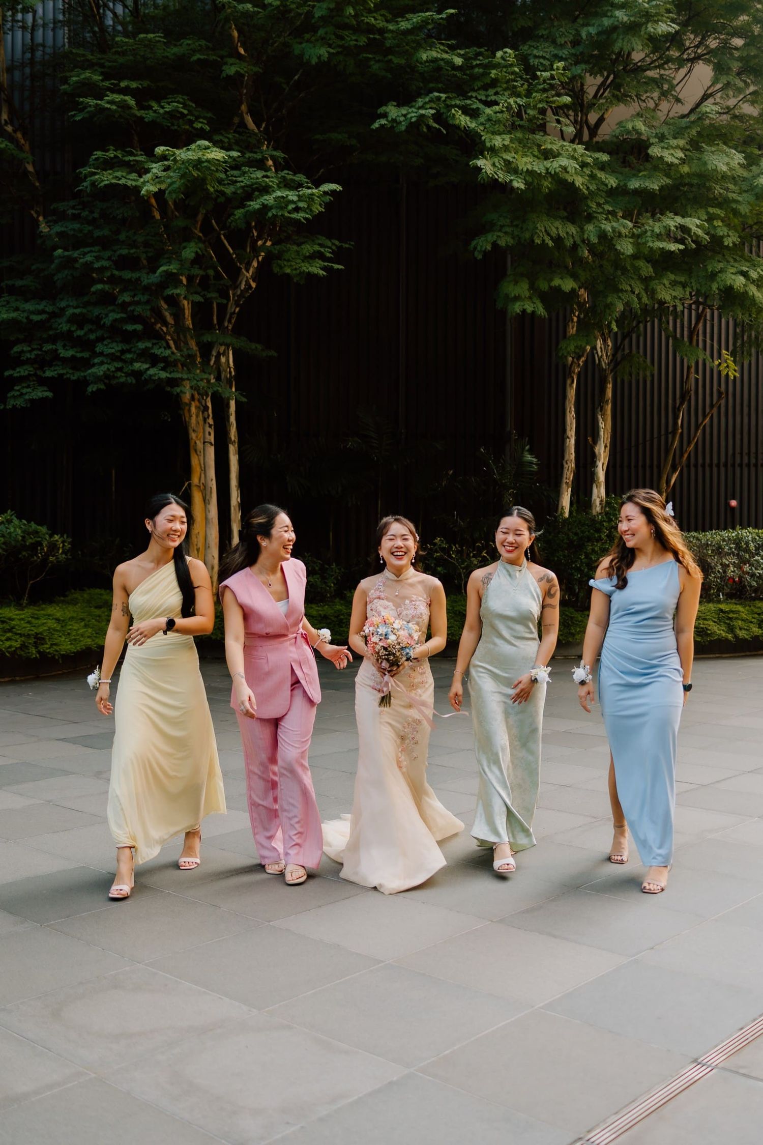 Bride and four bridesmaids in pastel dresses walking together outdoors at a wedding venue.