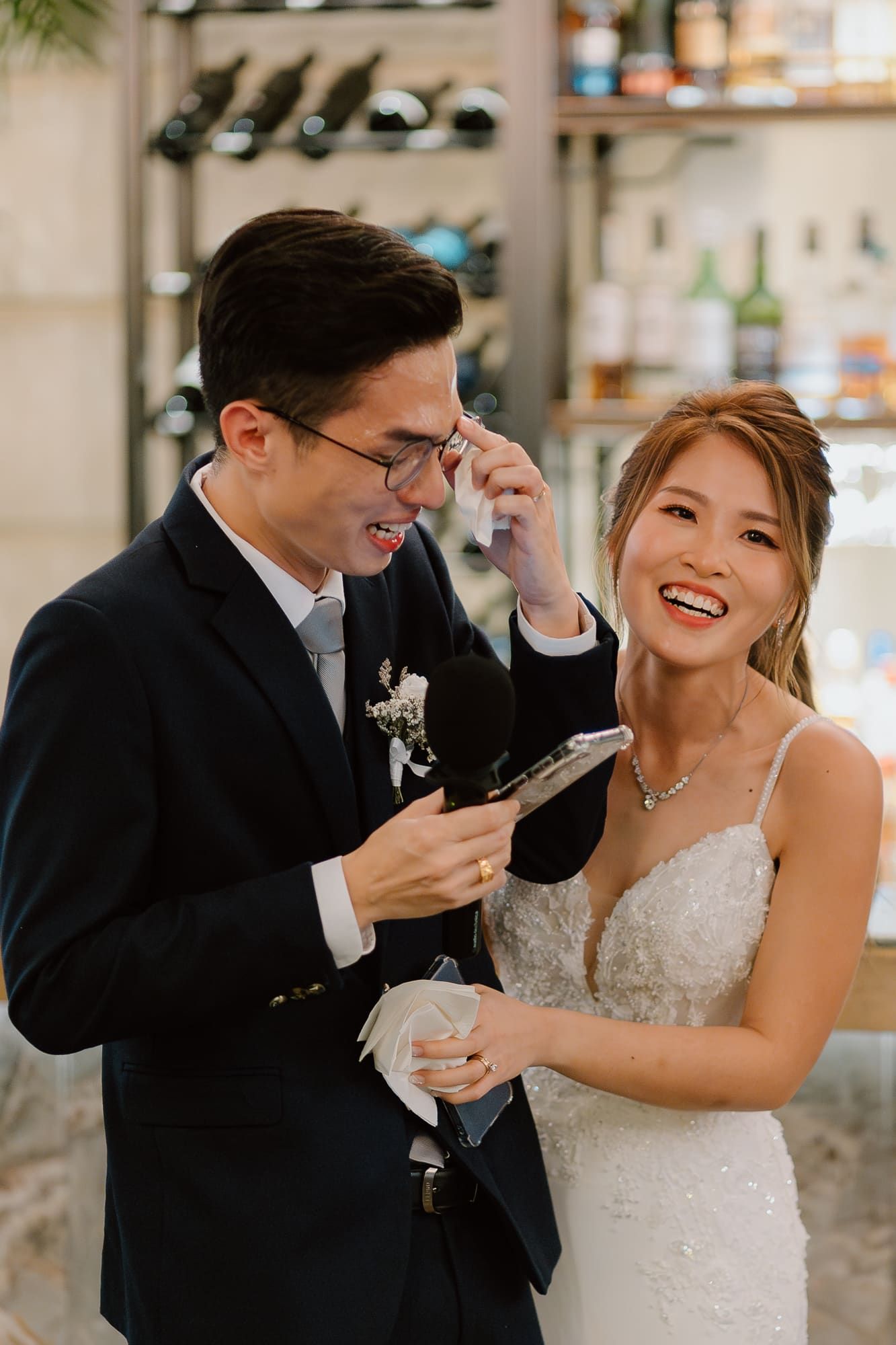 A joyful wedding moment shared between a couple laughing together at an indoor venue with a bar setting in the background.