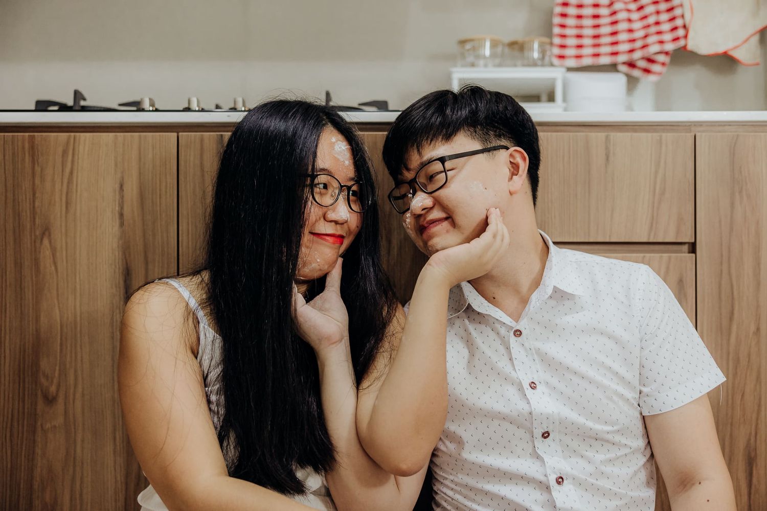 Couple sharing playful moments in a modern kitchen with wooden cabinets.