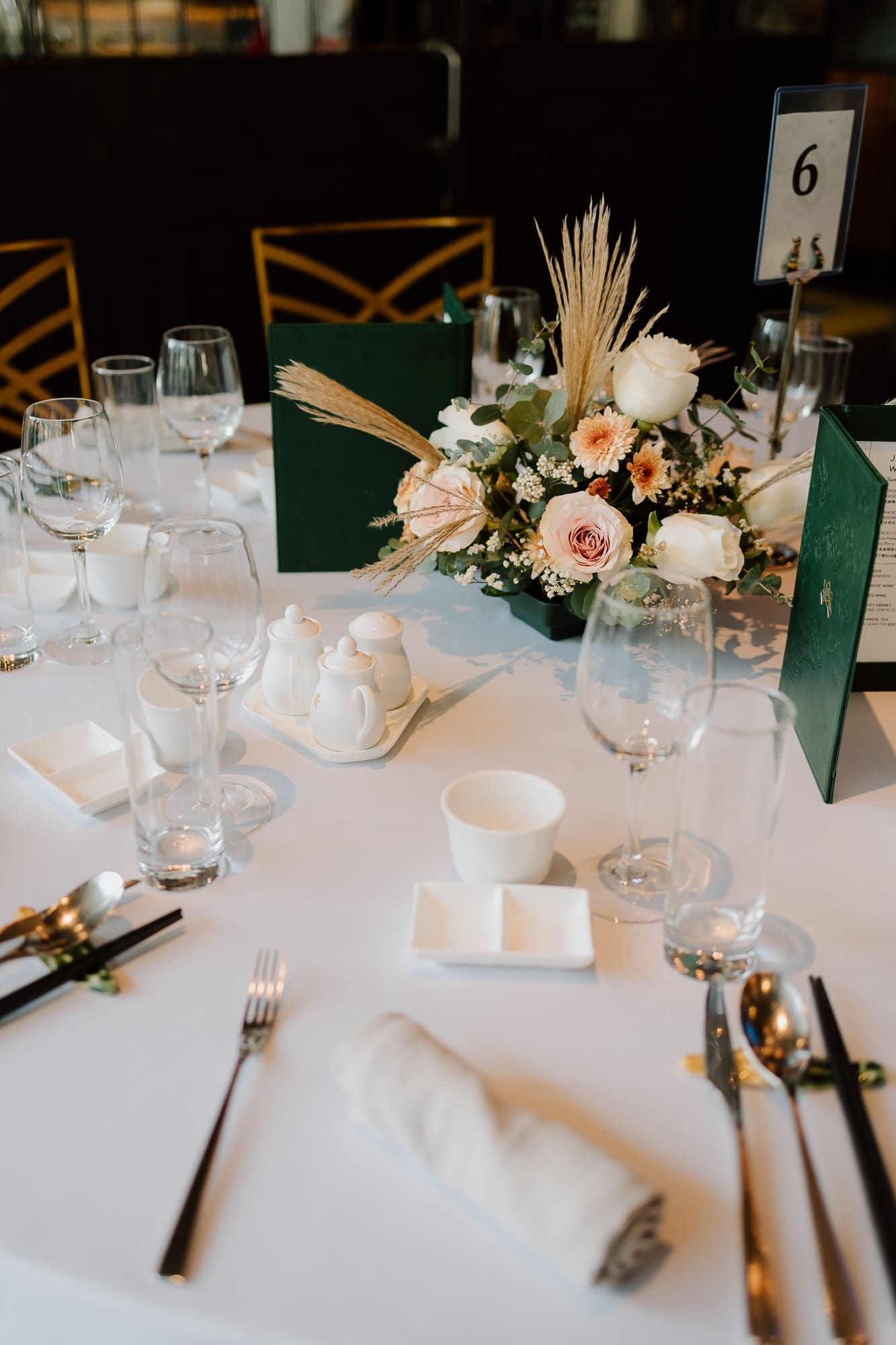 Elegant wedding table setting with white linens, emerald green accents, and a delicate floral centerpiece of roses and grasses.
