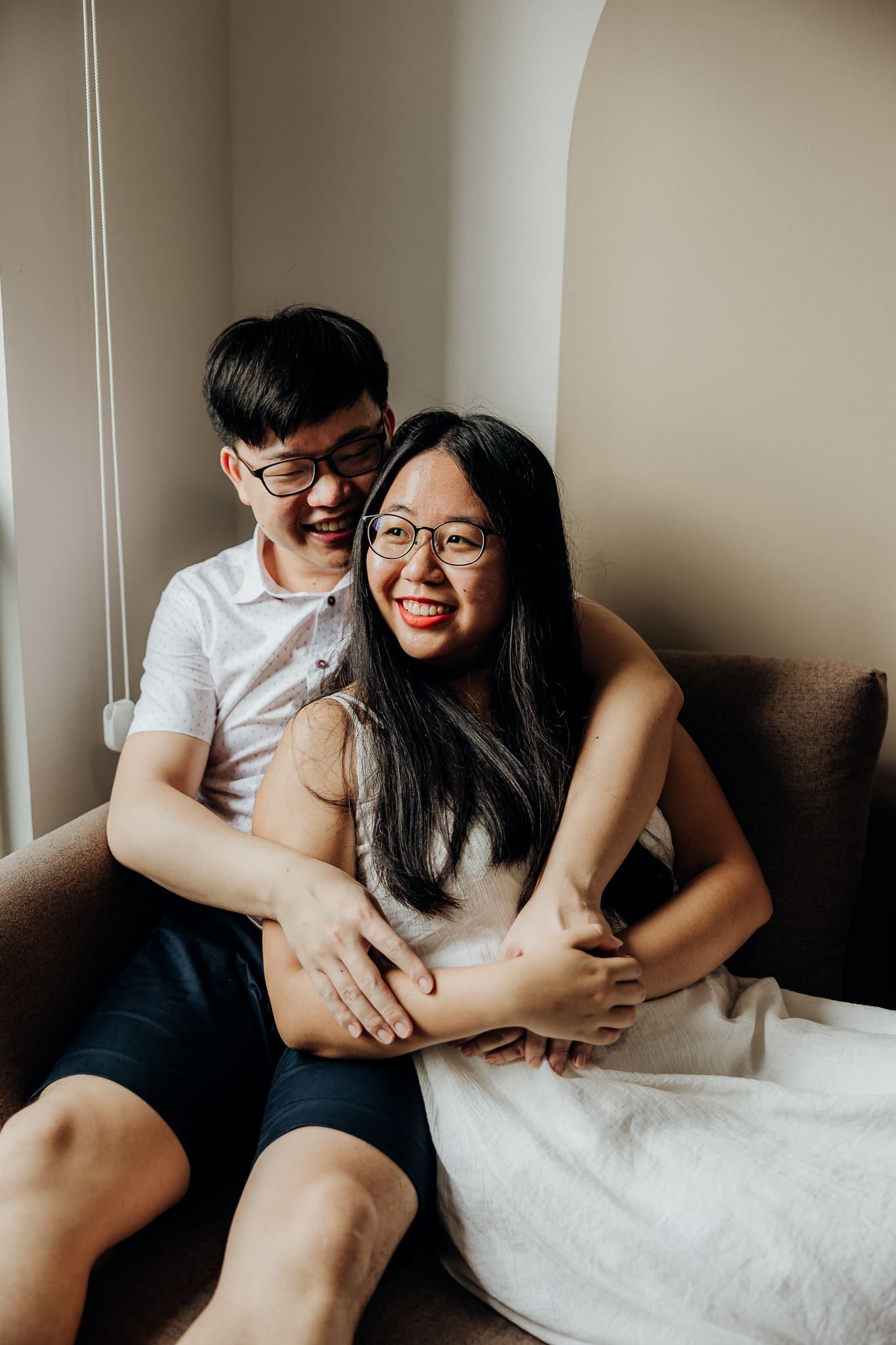 Candid moments of couple embracing on couch in natural window light.