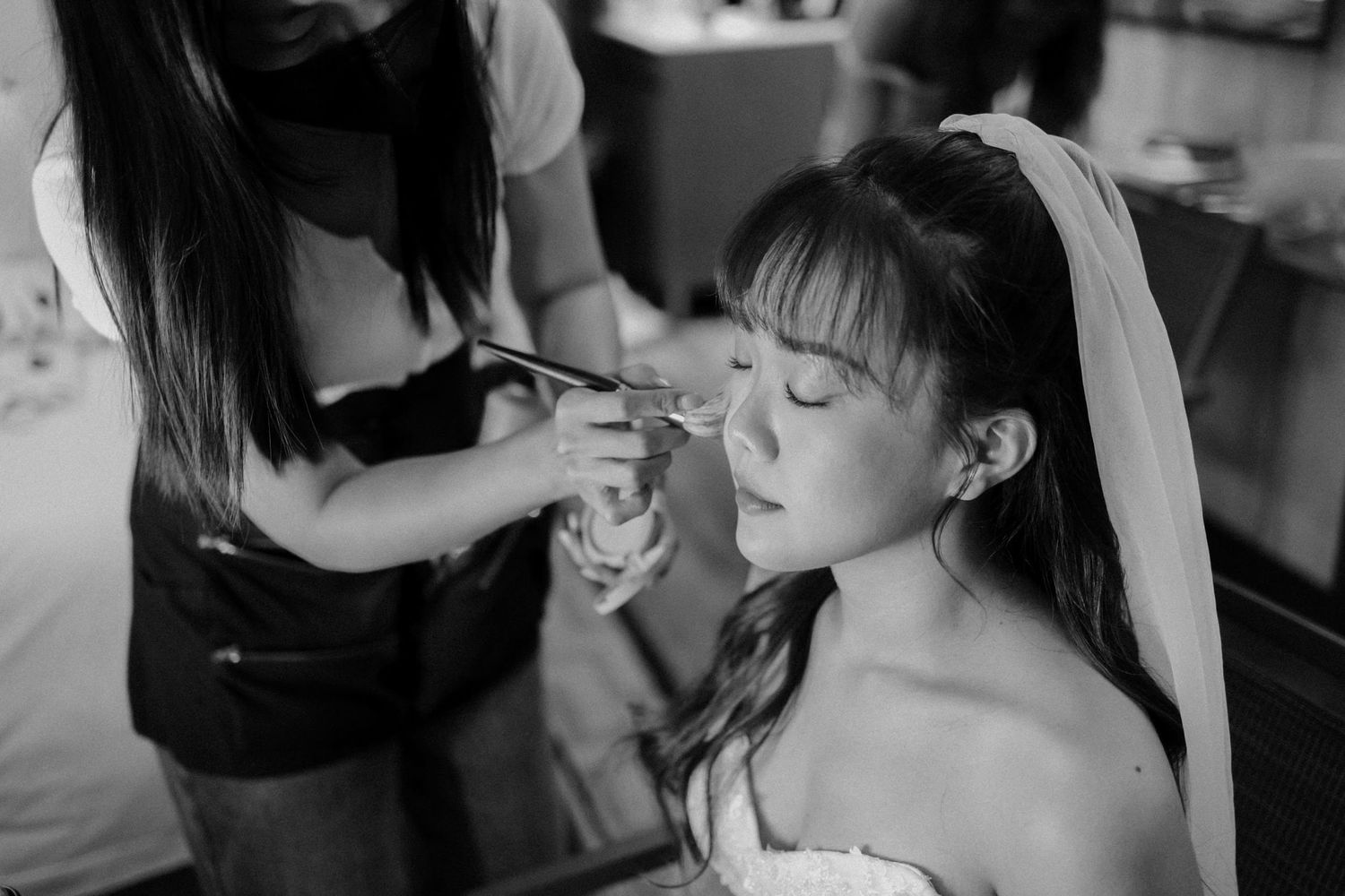Bride getting makeup applied by a professional artist in a black and white wedding preparation photo.