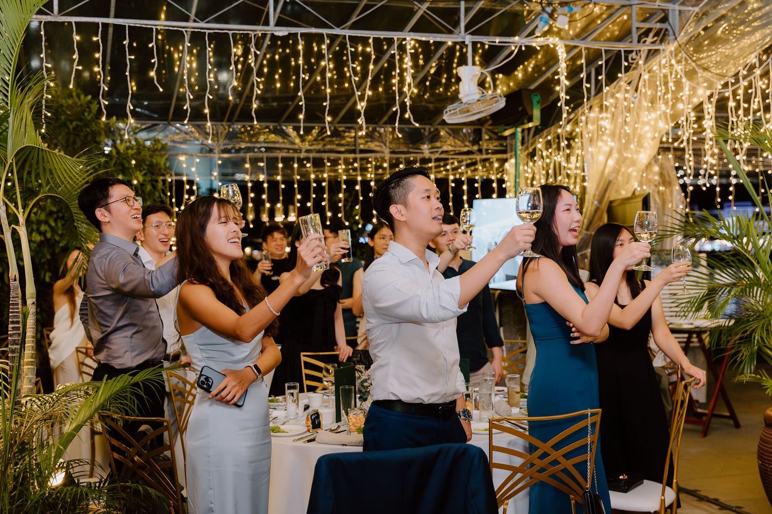 Couples dancing together in a tented reception area decorated with overhead string lights and drapery.