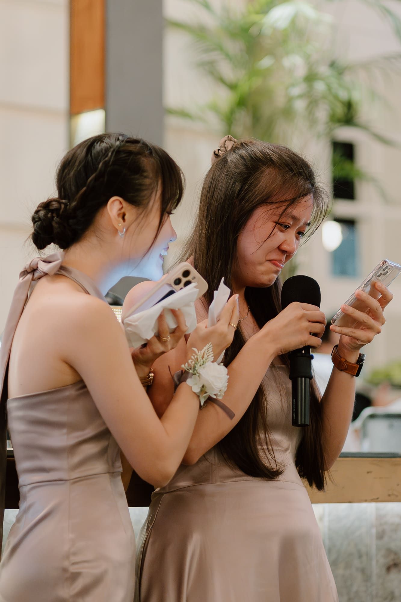 Bridesmaids in dusty rose dresses share an emotional moment while checking their phones at a wedding.