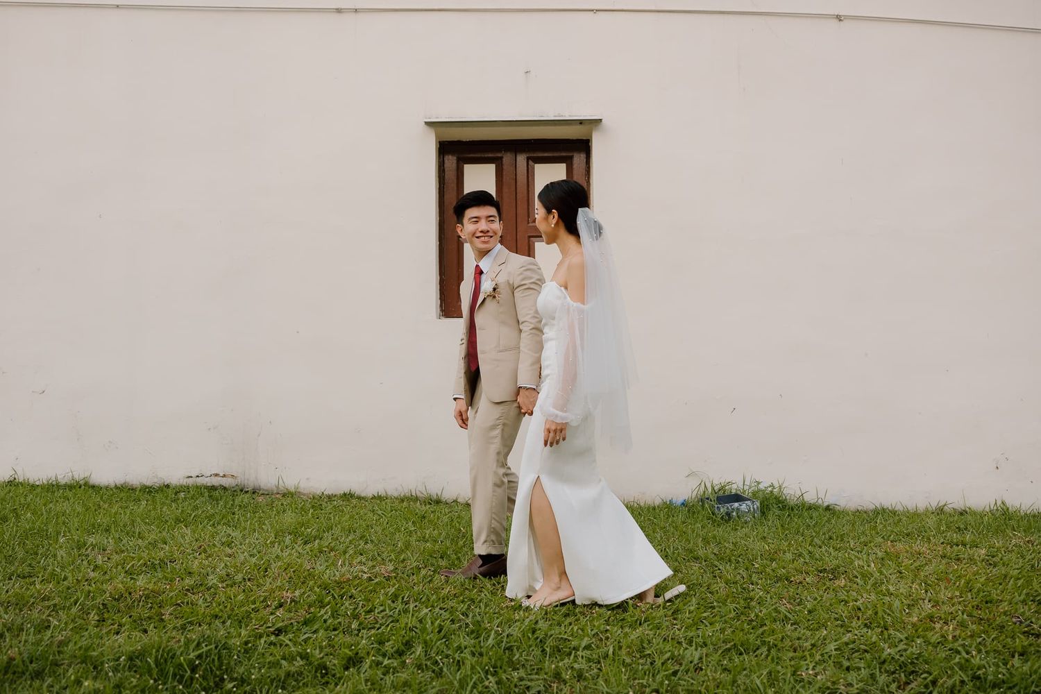Couple walking together on grass next to a white building.