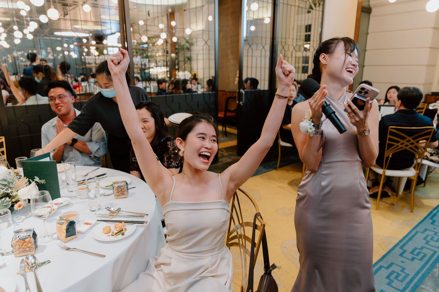Guests celebrating at a wedding reception raise their arms in joy as they participate in dinner activities.