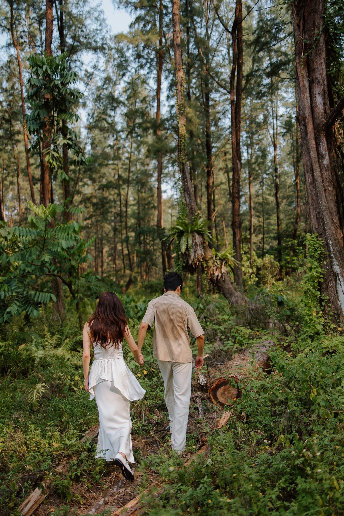 Couple holding hands walking through a lush green forest trail.