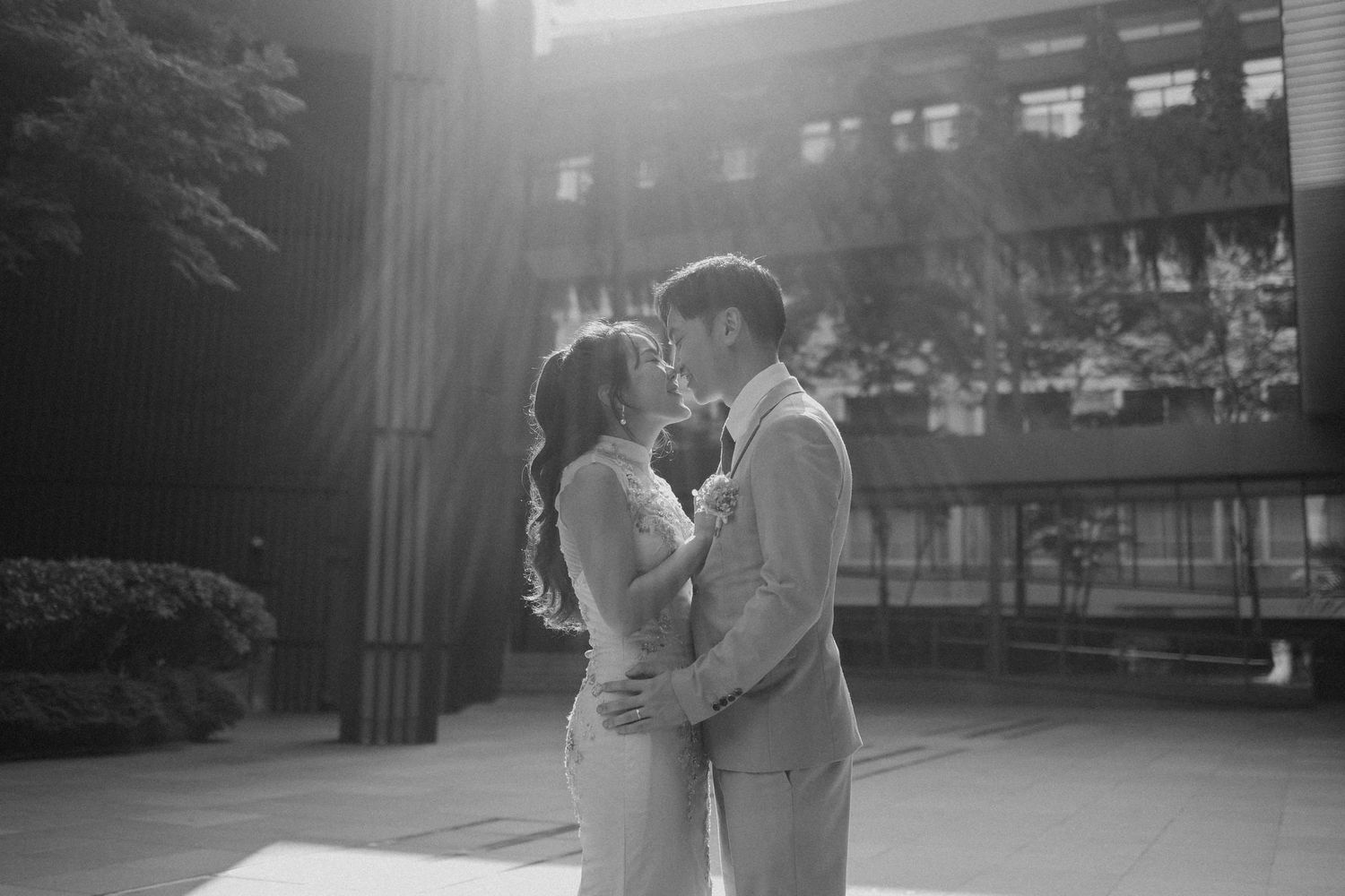 Black and white photo of a bride and groom sharing a romantic moment outdoors near a modern building.