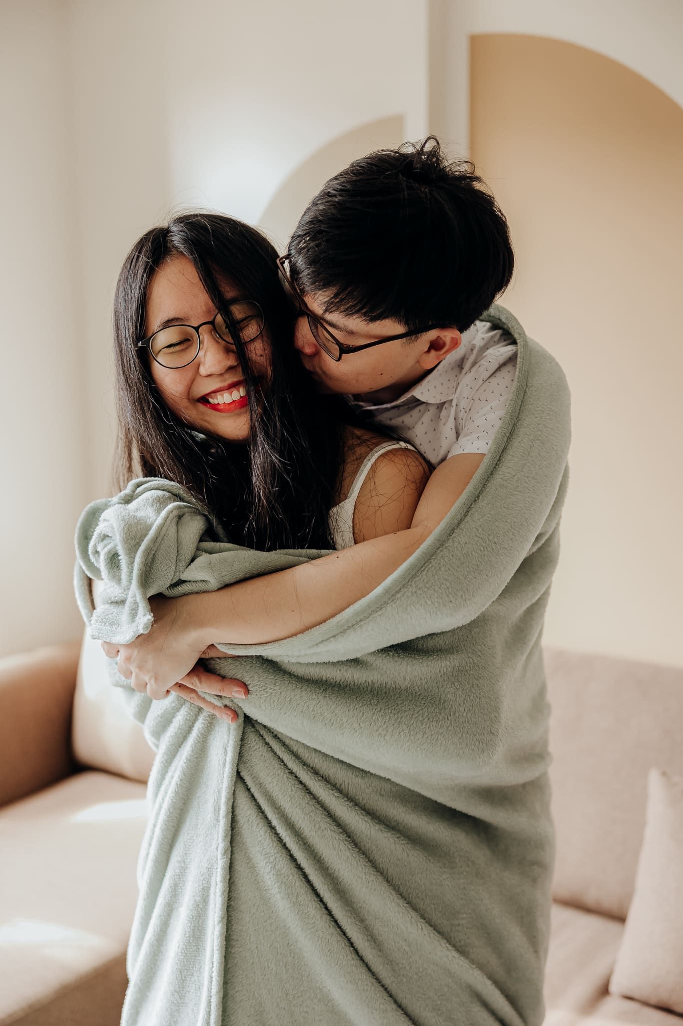 Couple wrapped in a cozy sage green blanket sharing loving moments together.