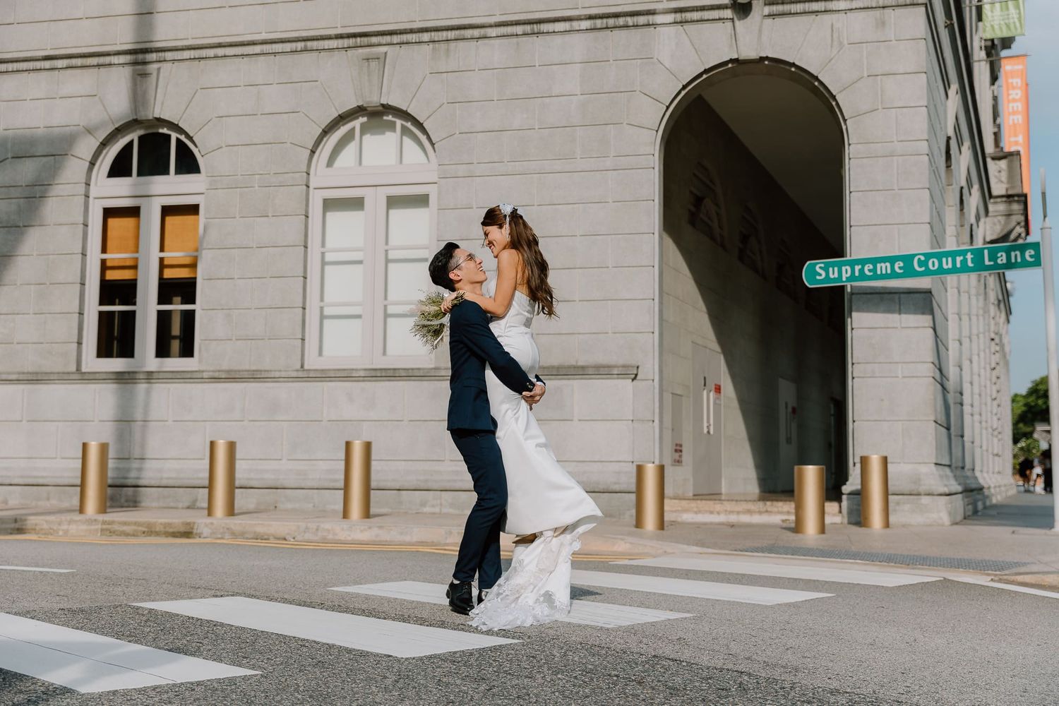 A couple shares a romantic embrace on a city street corner with classic architecture in the background.