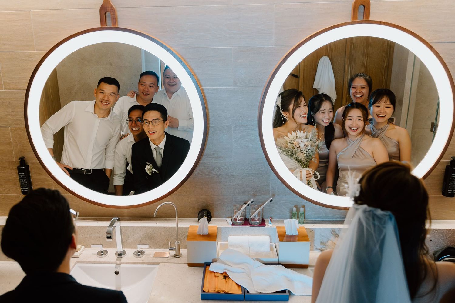 Wedding party members getting ready in front of round bathroom mirrors with blue accents on the countertop.