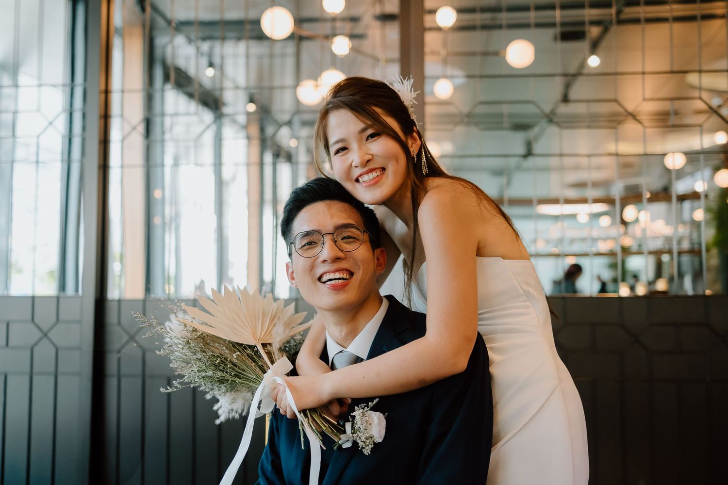 Smiling couple looks at each other during emotional wedding ceremony in modern industrial venue with hanging lights.