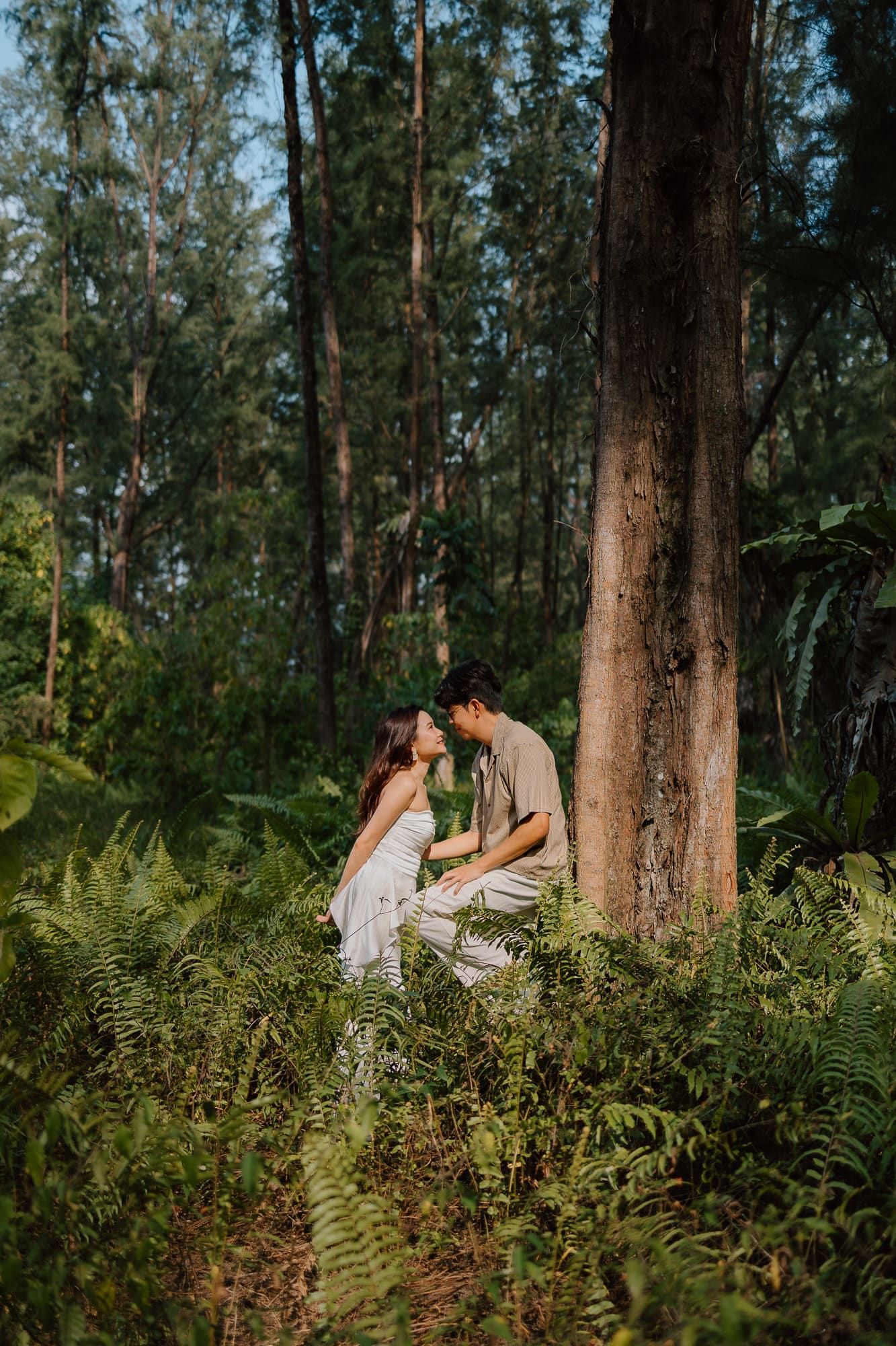Couple sharing a romantic moment among lush ferns and tall trees in a tropical forest setting.
