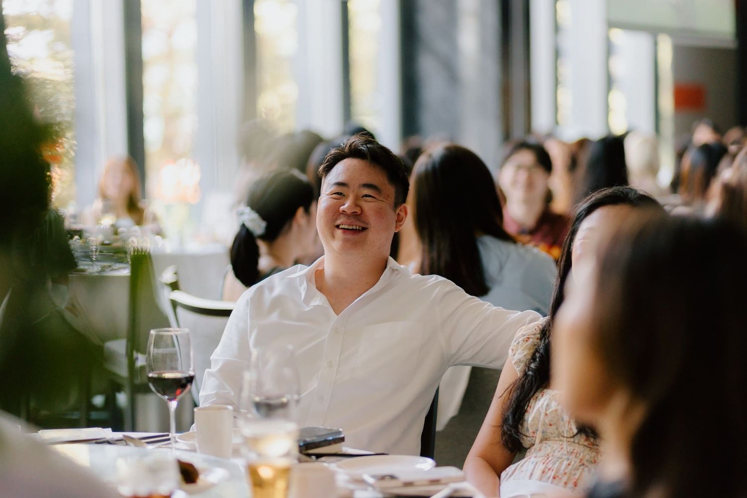 Man in white shirt laughing joyfully at a restaurant dinner event surrounded by guests.
