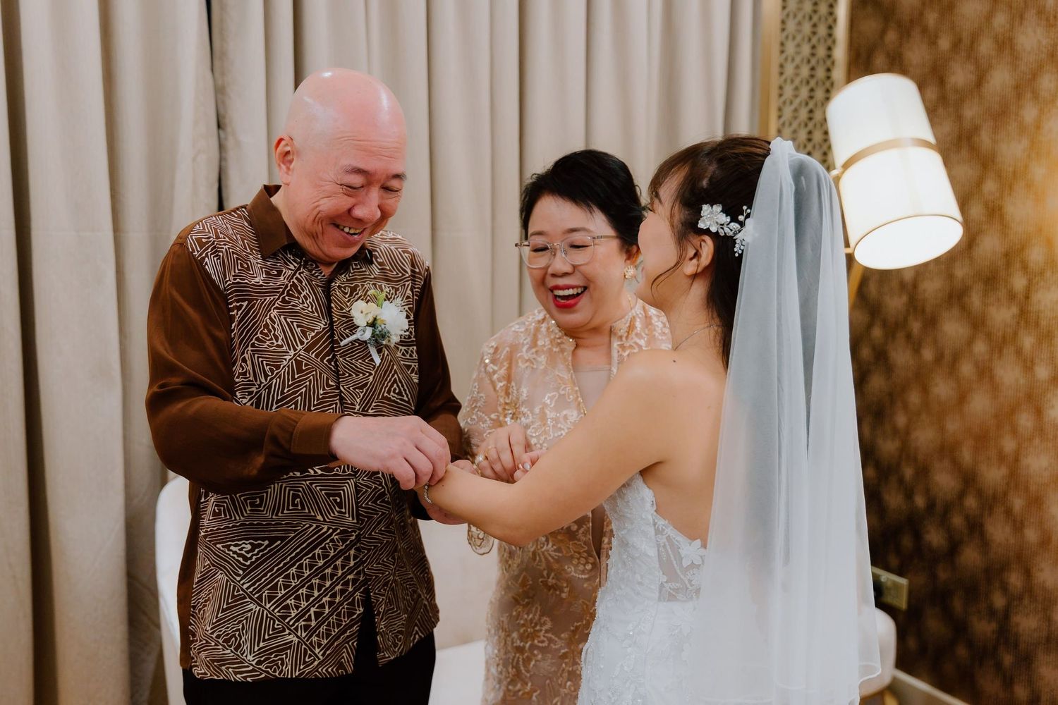 Joyful bride in white veil shares a happy moment with smiling elderly couple in elegant attire at a wedding celebration.