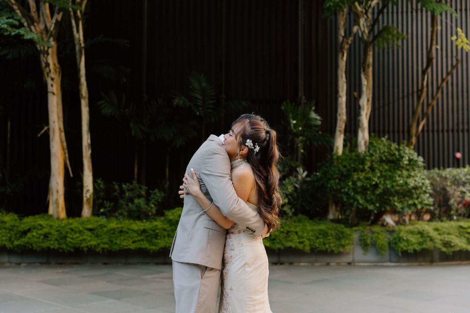 Bride and groom share romantic embrace outdoors, bride wearing floral hair accessories and lace gown.