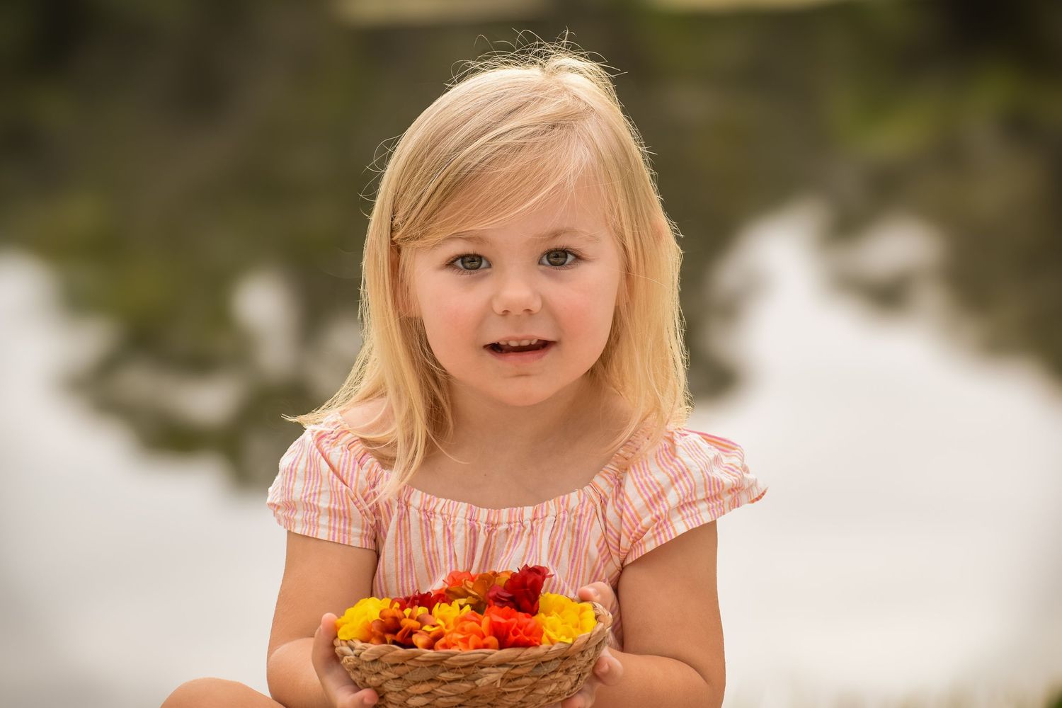 Cute blonde little girl holding a wicker basket filled with red and orange flowers.