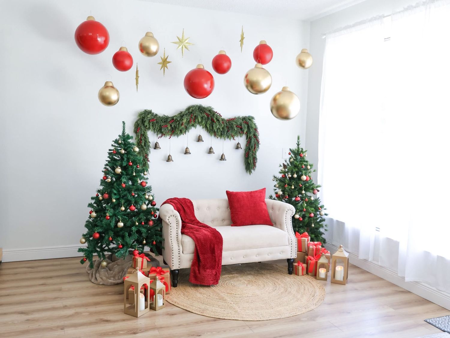 Festive living room with two Christmas trees, red and gold ornaments, garland, gifts, and a white sofa with red accents.