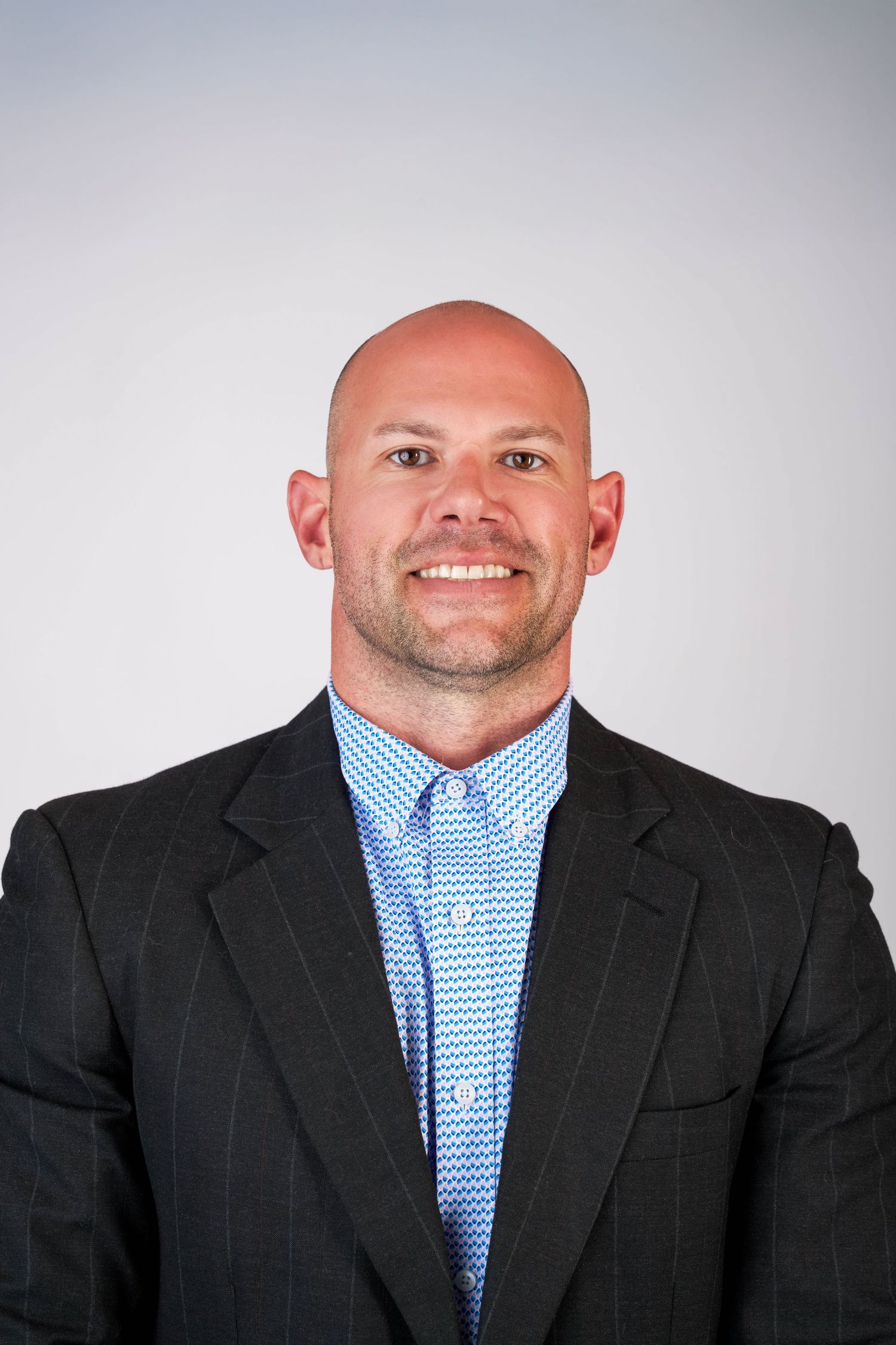 Smiling bald businessman in dark suit, blue shirt, and patterned tie poses for professional headshot photo In Bryan college station Texas.