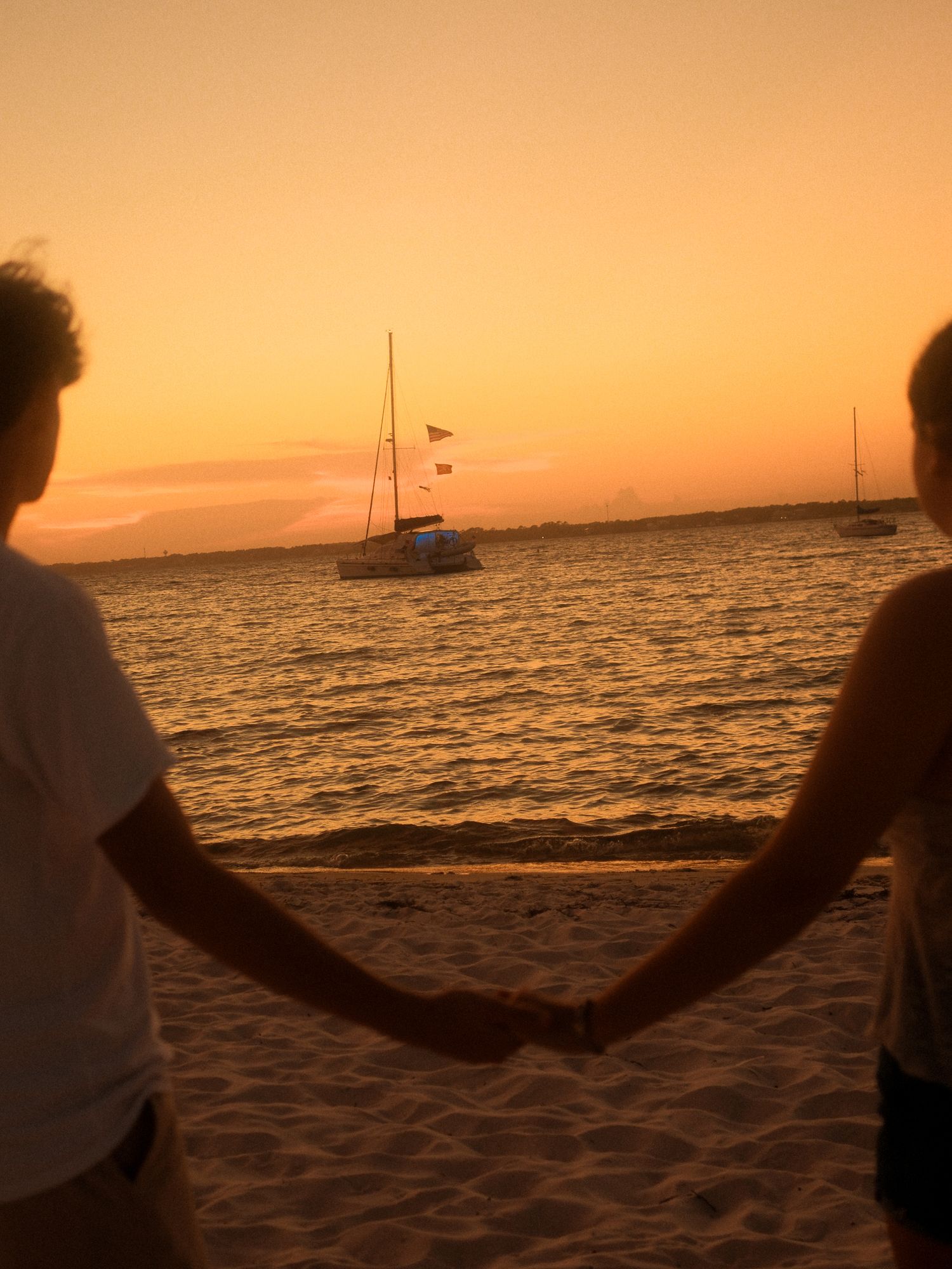 Sawyer and Fiona holding hands on the beach at sunset.