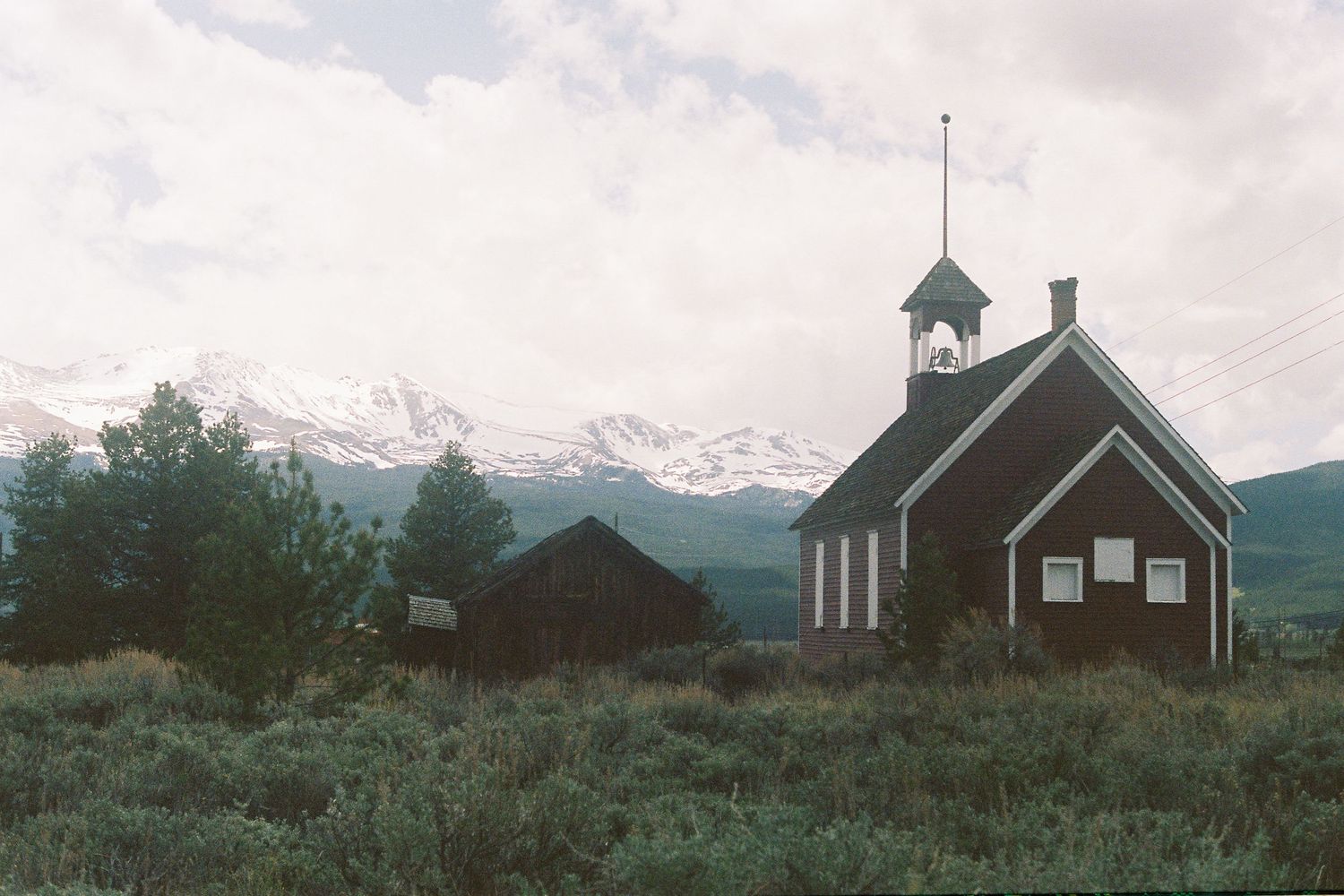 An abandoned schoolhouse in the Rocky Mountains with a cloudy sky overhead.