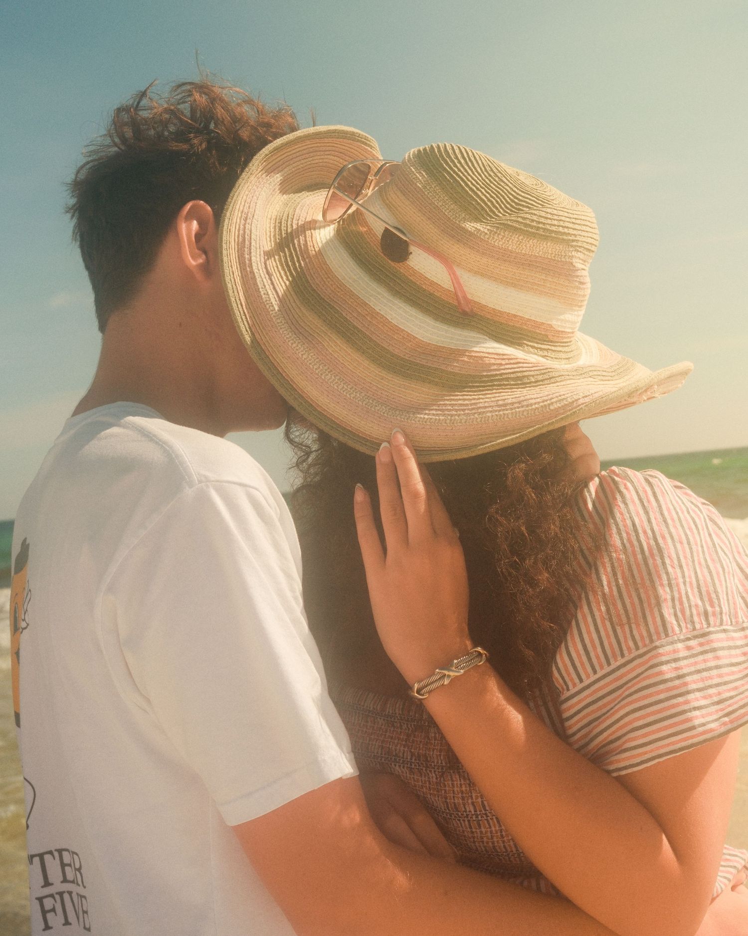 Sawyer and Fiona holding each other as Fiona tips her hat on the beach.
