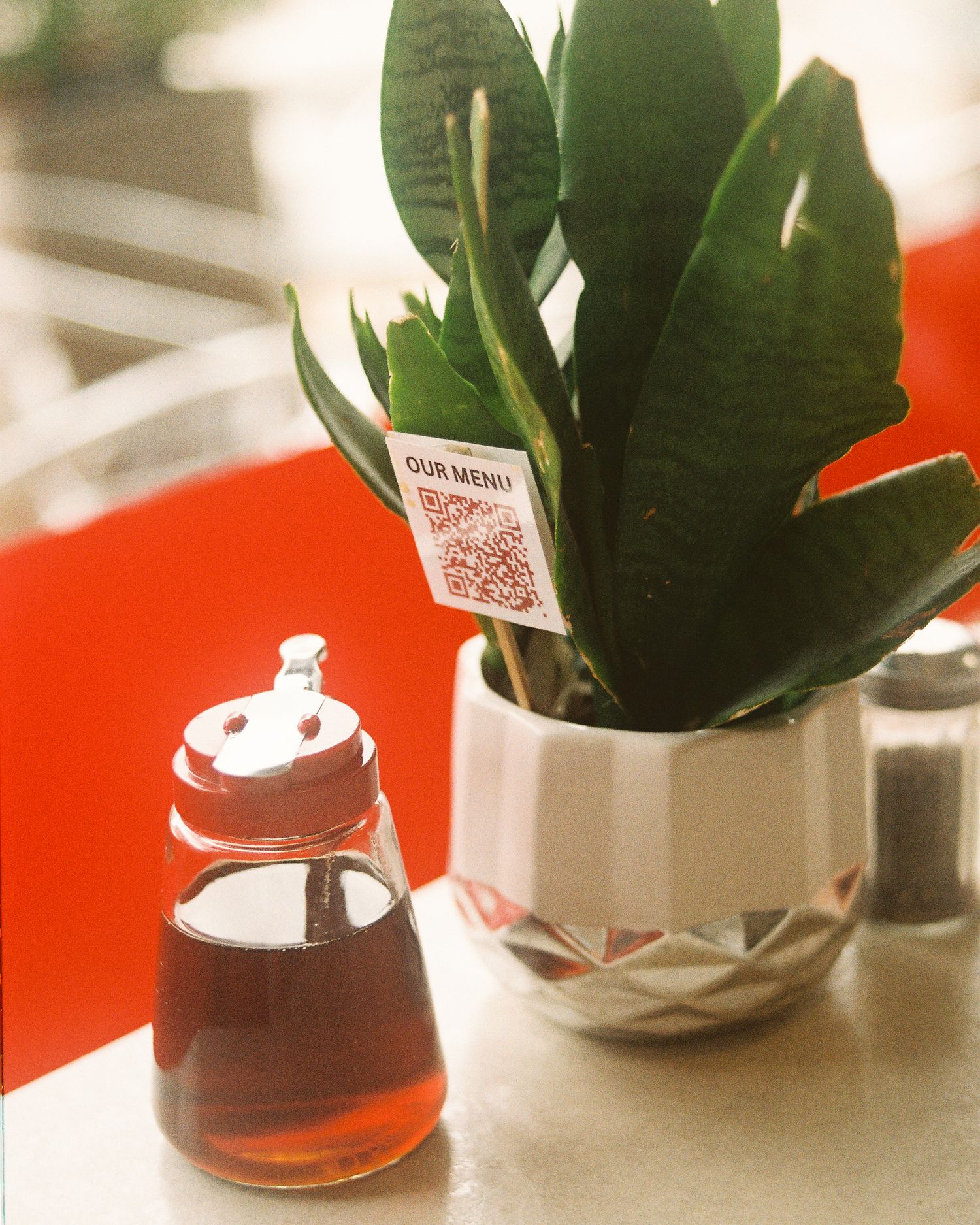 At The Corner tabletop with a plant, menu QR code, and syrup container.