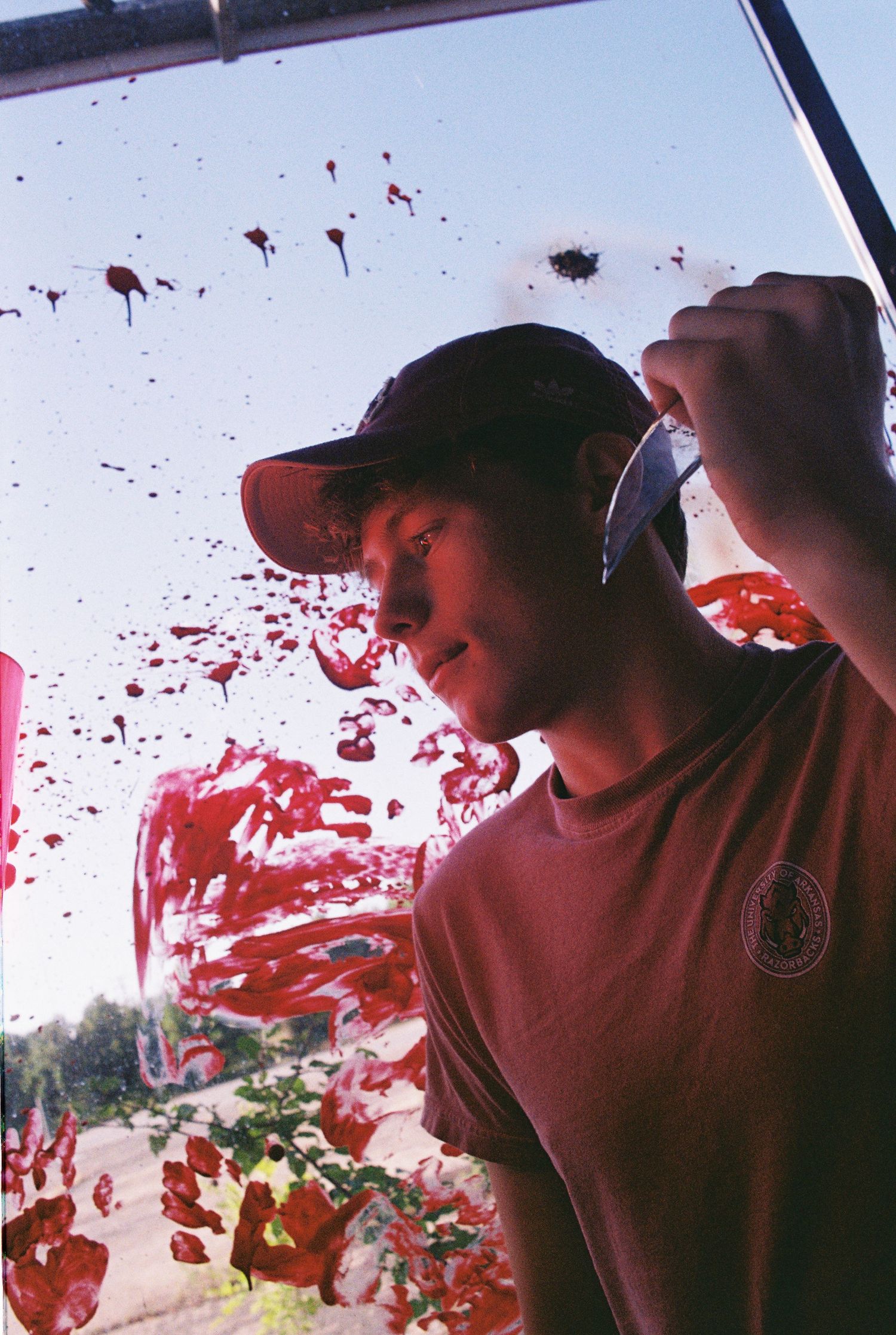 Person holding glass blade with red paint on the window behind them.