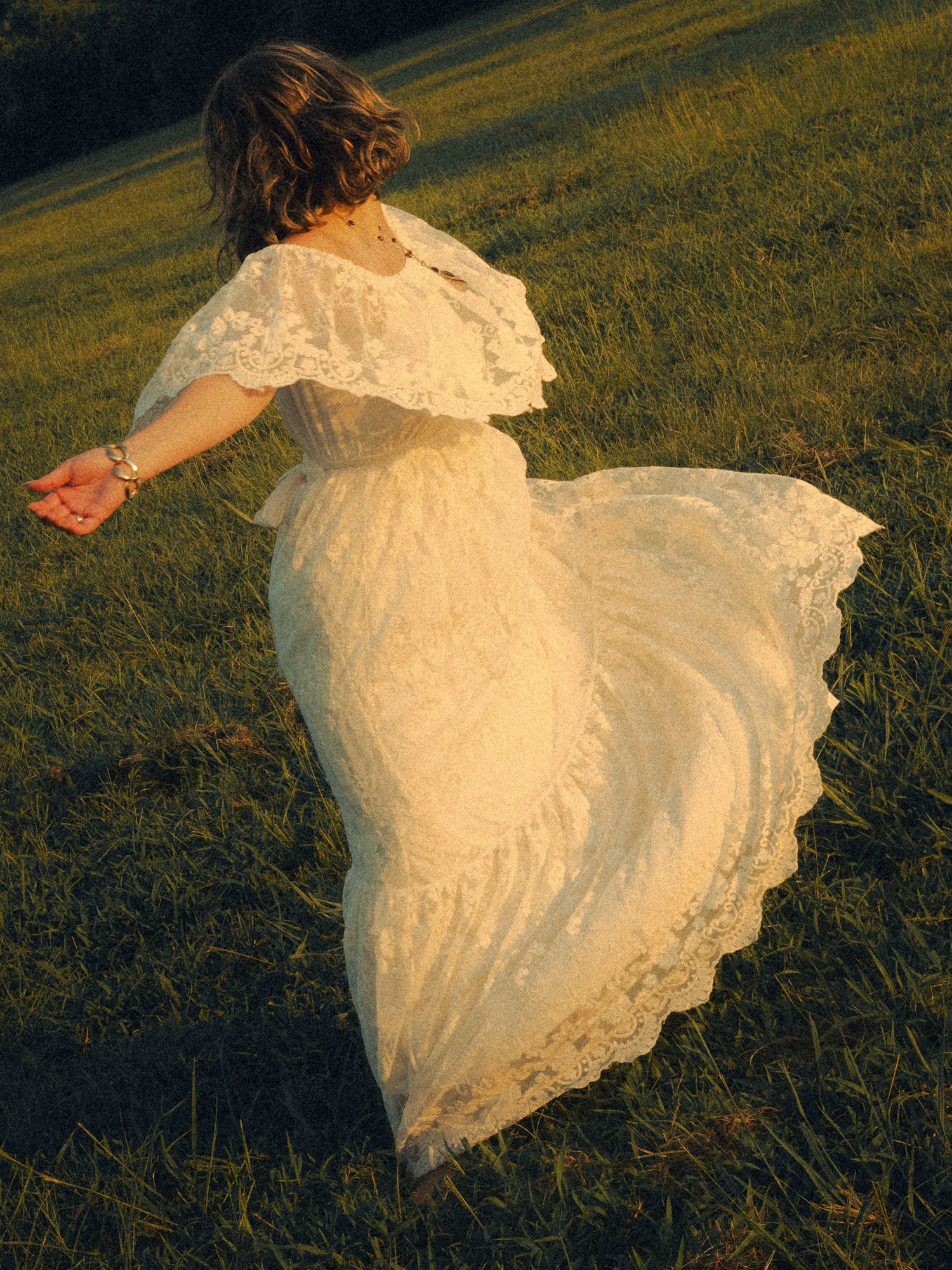 Caroline spinning in a white dress in a field.