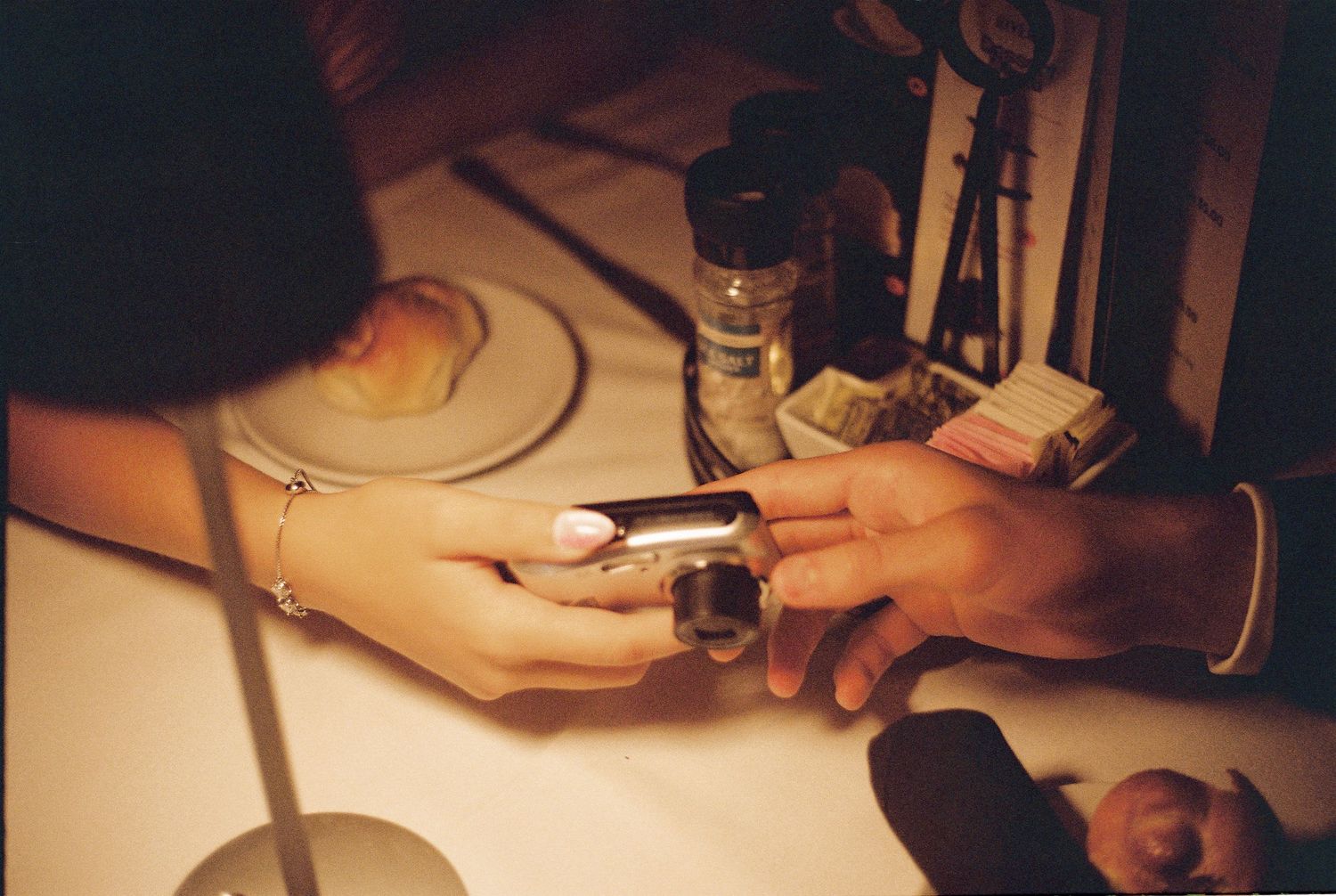 Two hands holding onto a small digicam underneath dim restaurant lighting.