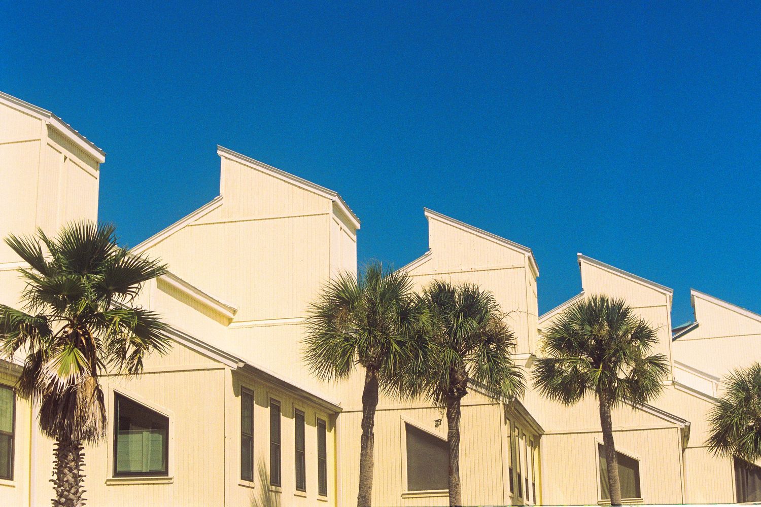 Yellow condos contrasting a deep blue sky with palm trees in front.