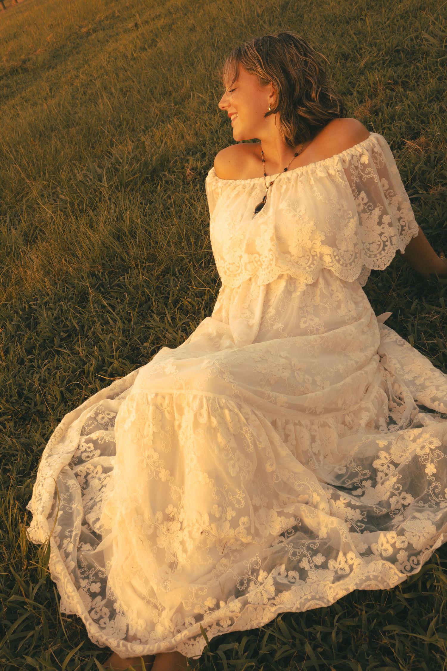 Caroline sitting in a white dress in a field.